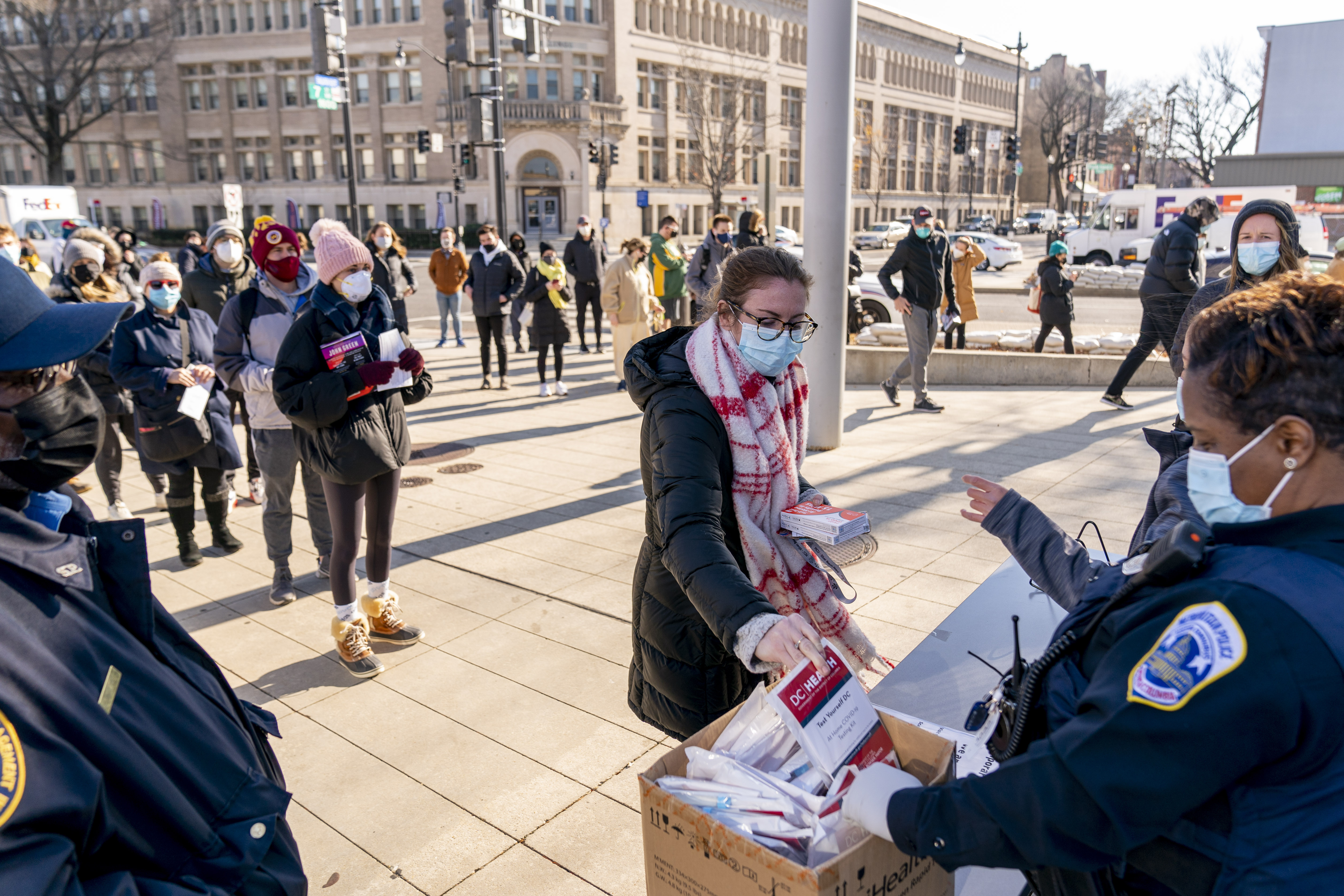 A woman receives at-home COVID-19 test kits after waiting in a long line that snakes multiple times around the Shaw Library in Washington