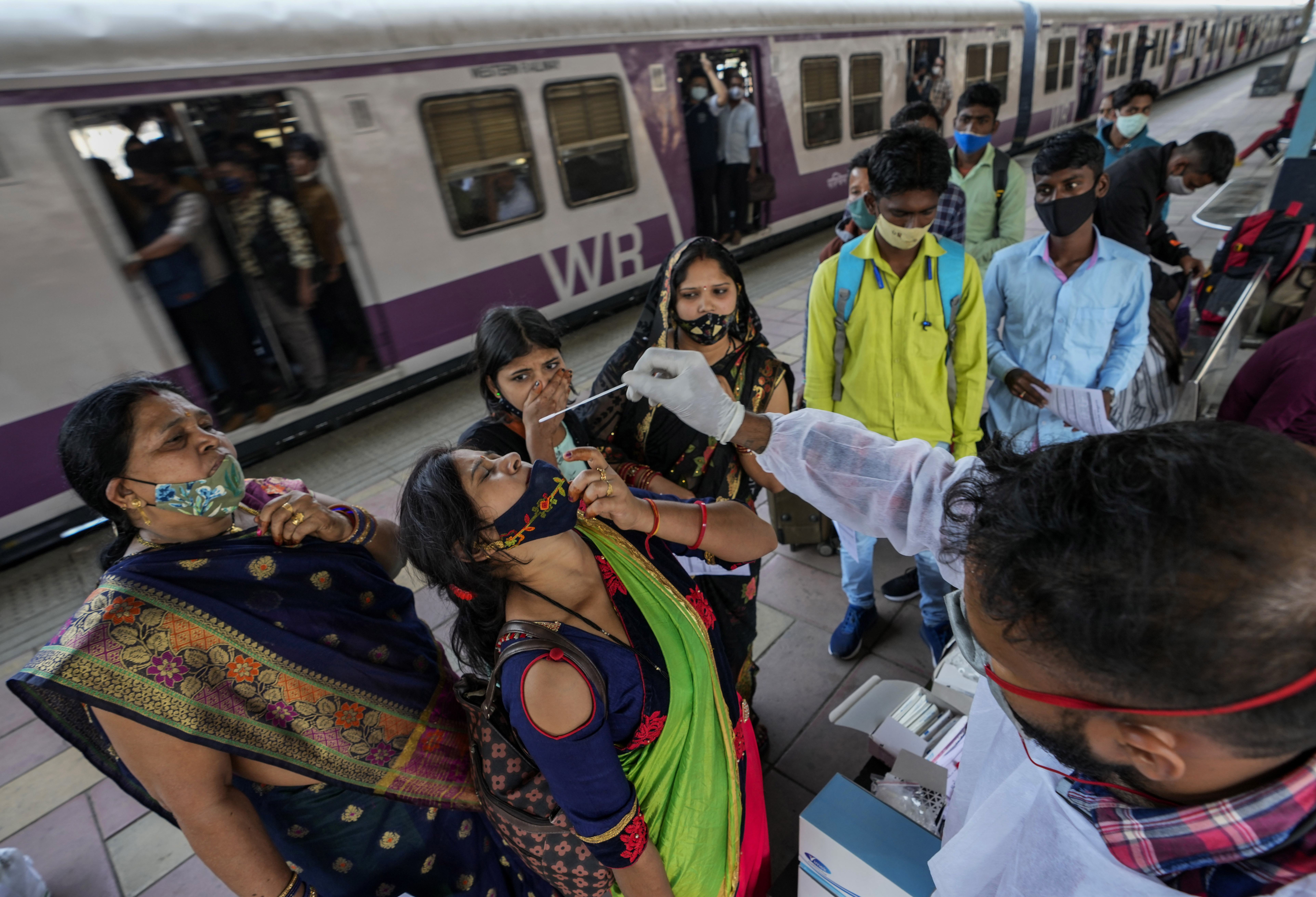 A health worker collects a swab sample from a traveler at a train station in Mumbai