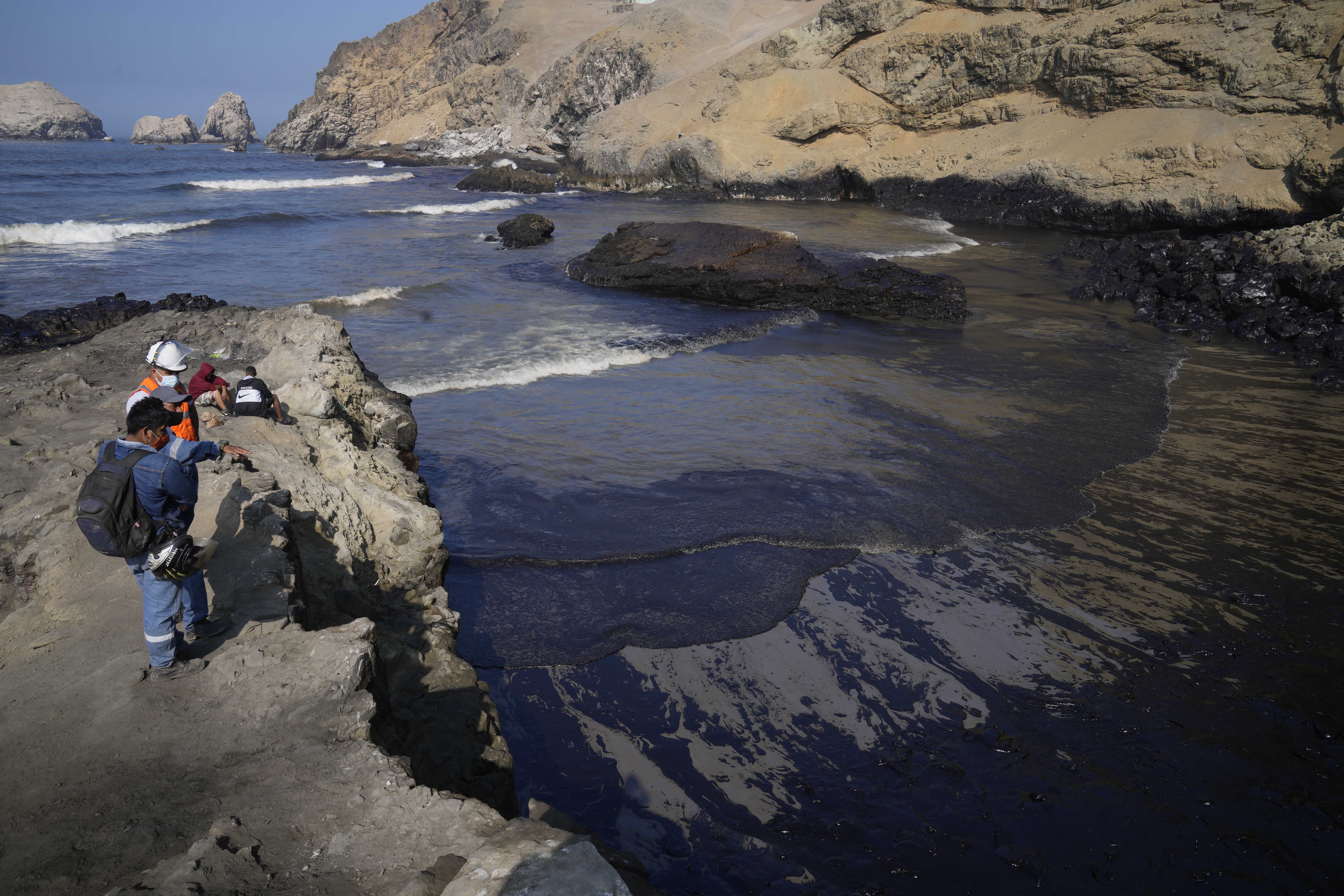 Workers look at the oil in the waters of Cavero Beach in Ventanilla, Callao, Peru, on January 18