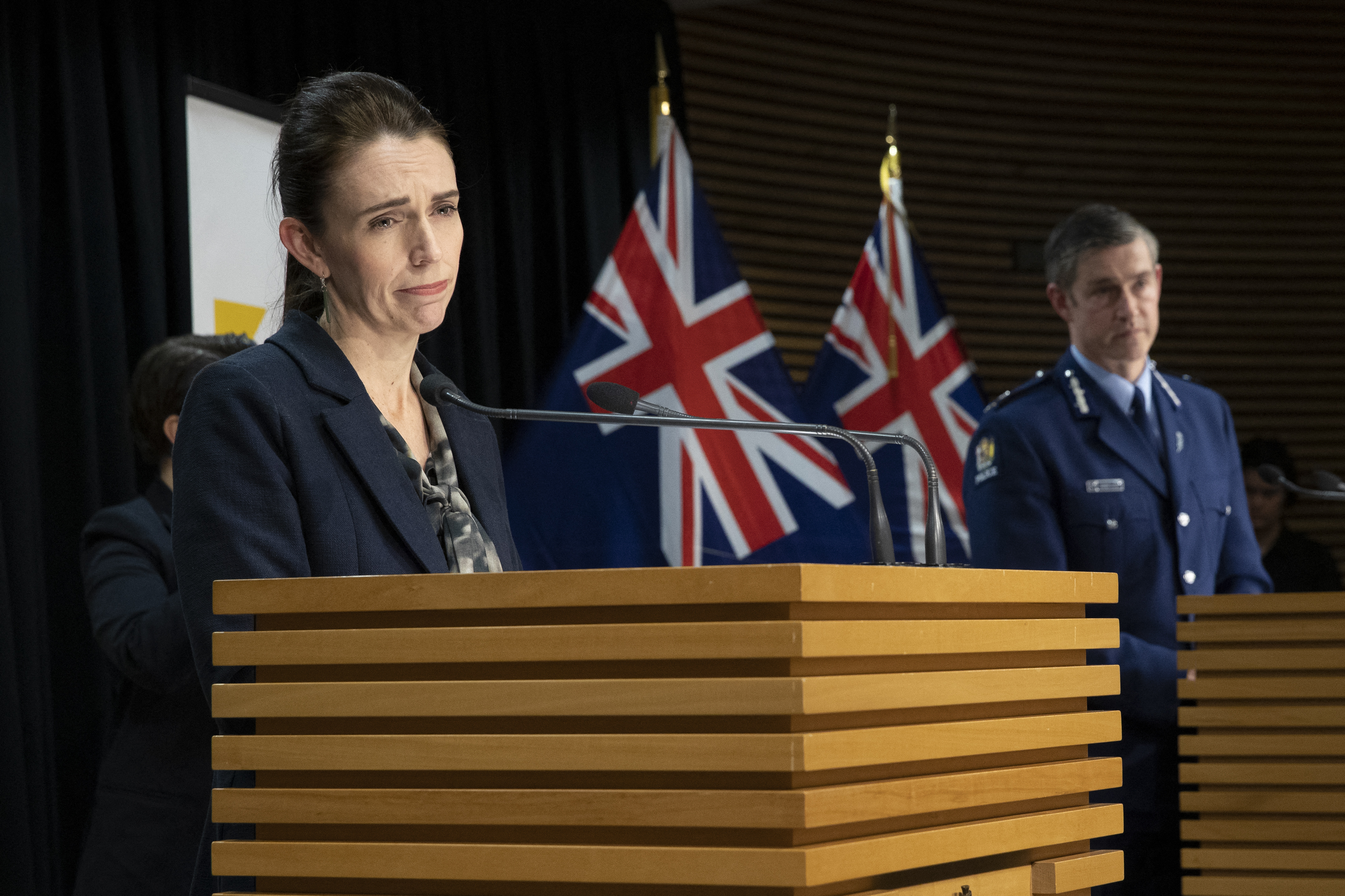 New Zealand Prime Minister Jacinda Ardern speaking to the media from a lectern with New Zealand flags behind