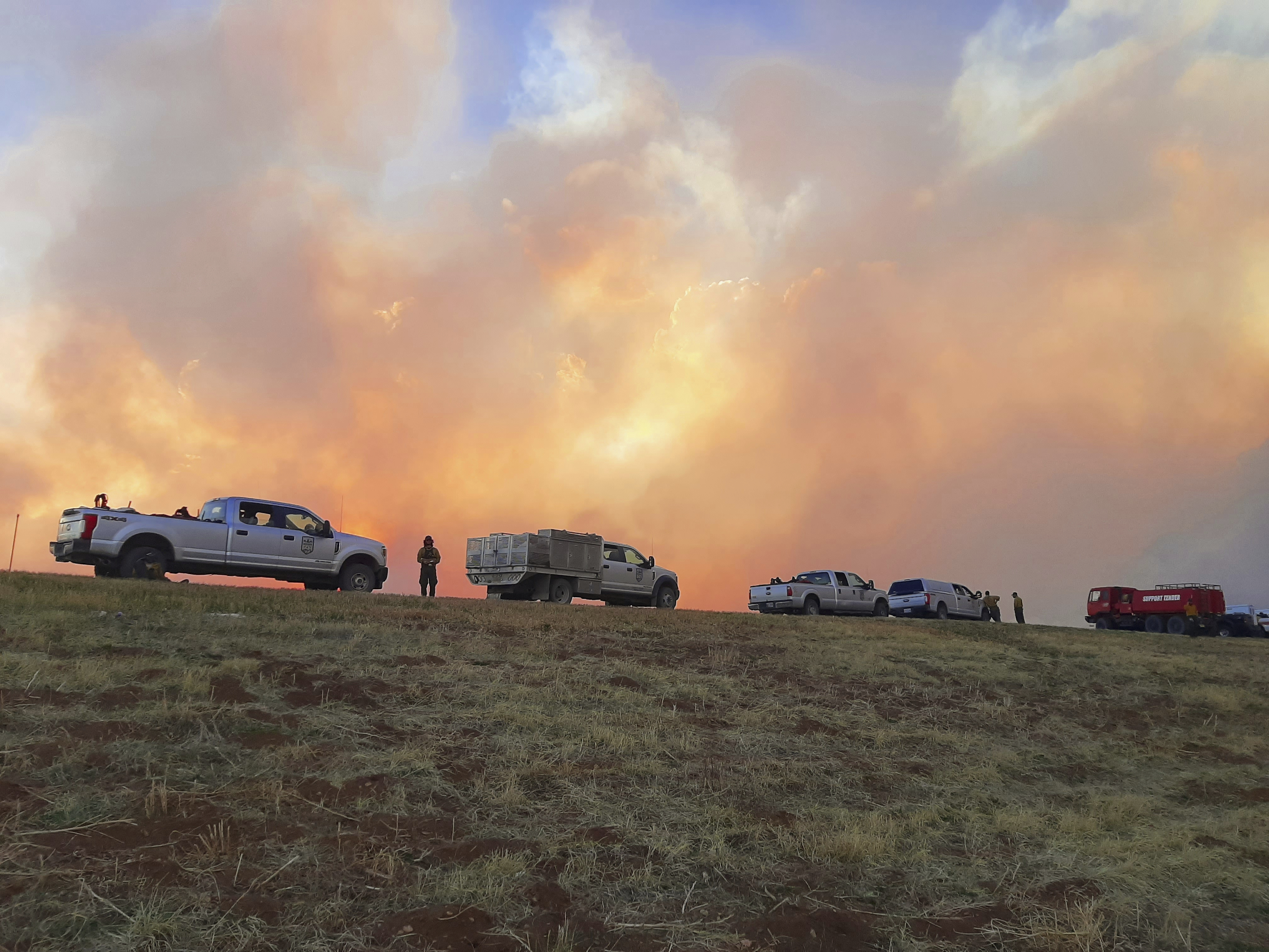 Fire is seen in the background behind several cars and vans