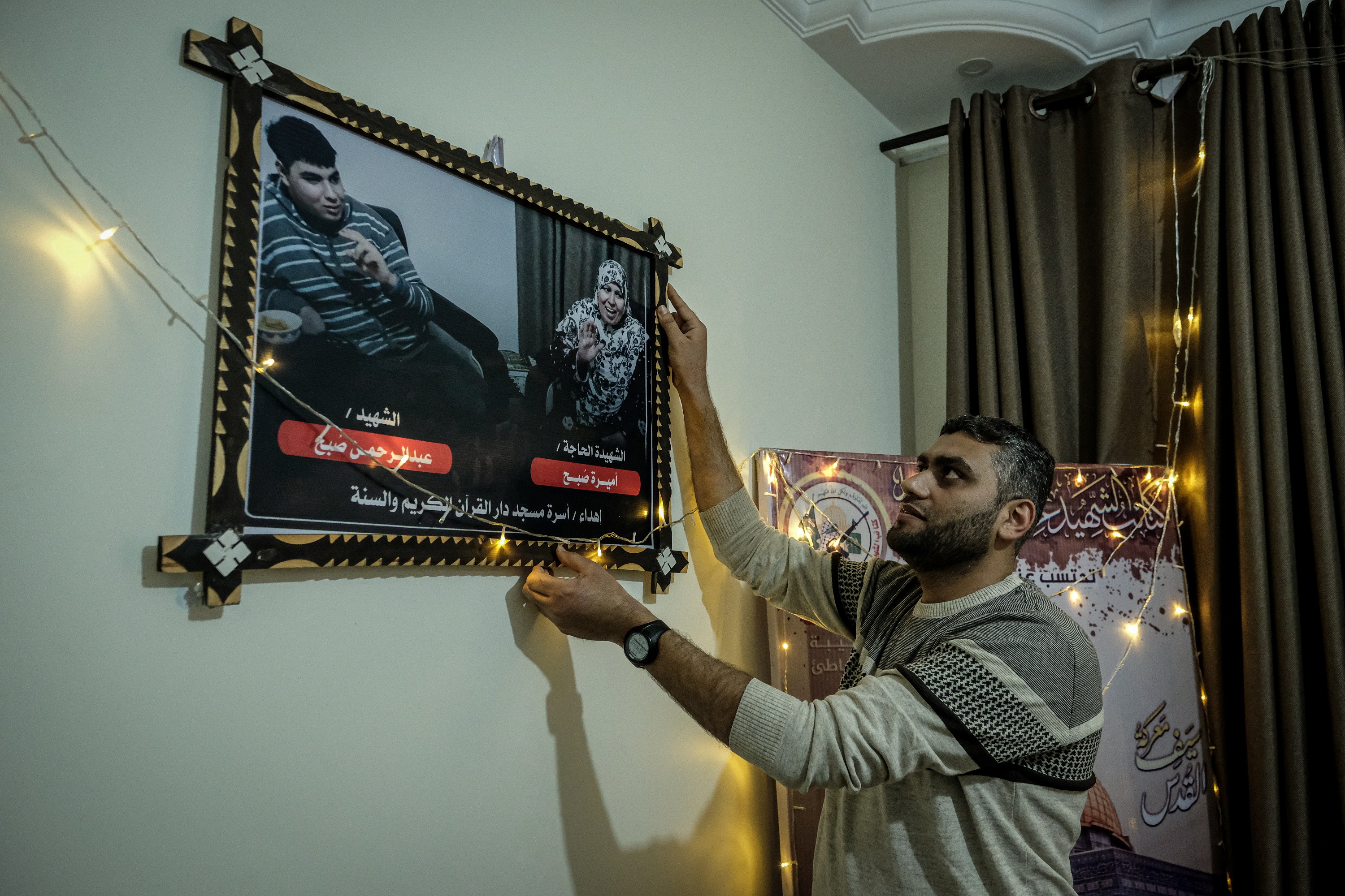 Muath Soboh hangs a photo of his mother, Amira, and his brother, Abdelrahman, who were killed in an Israeli air attack on their home last May