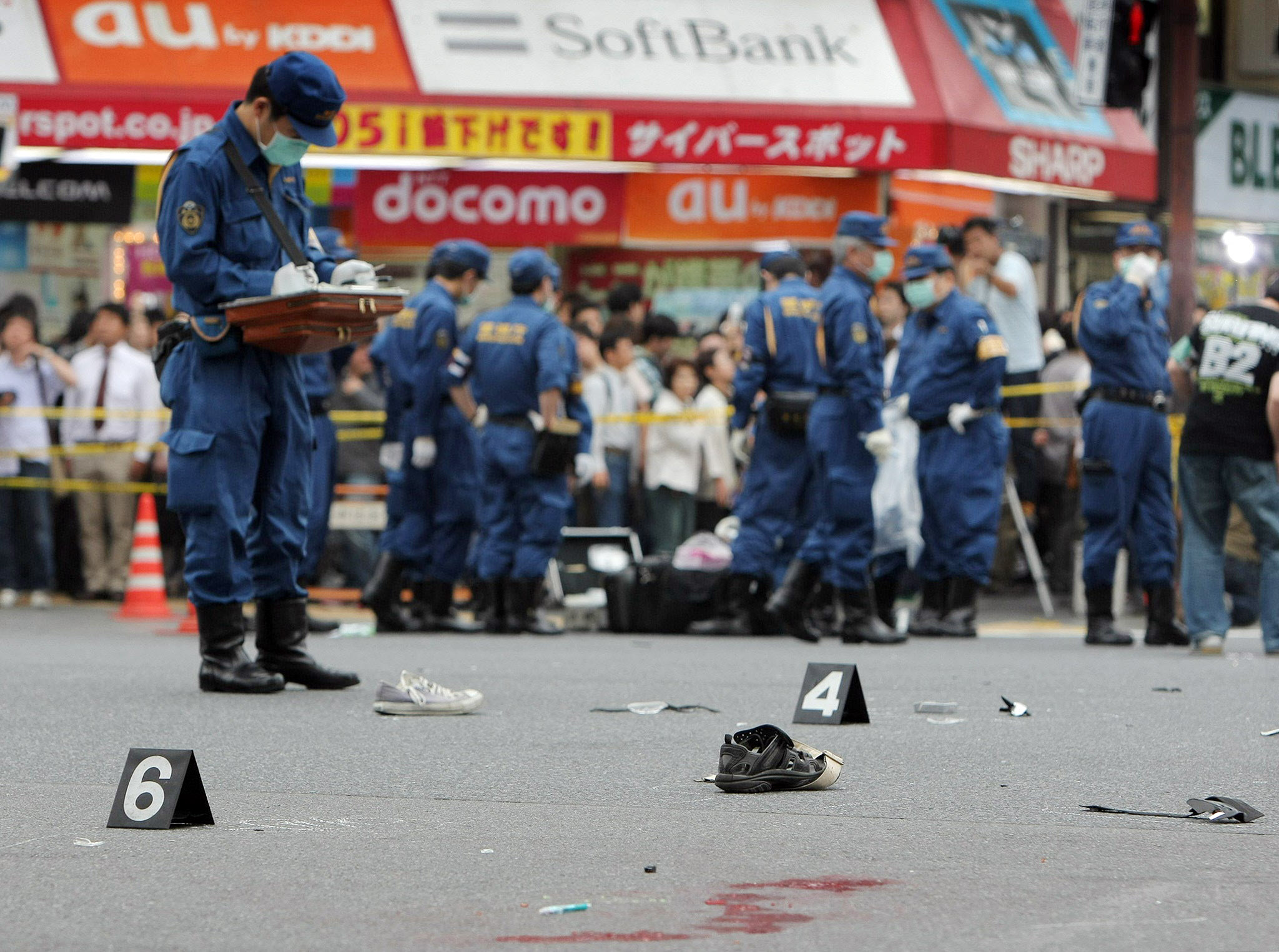 Police on a blood-stained street in Akhibara investigate the aftermath of Kato's stabbing attack watched by a crowd of onlookers in Tokyo, Japan.