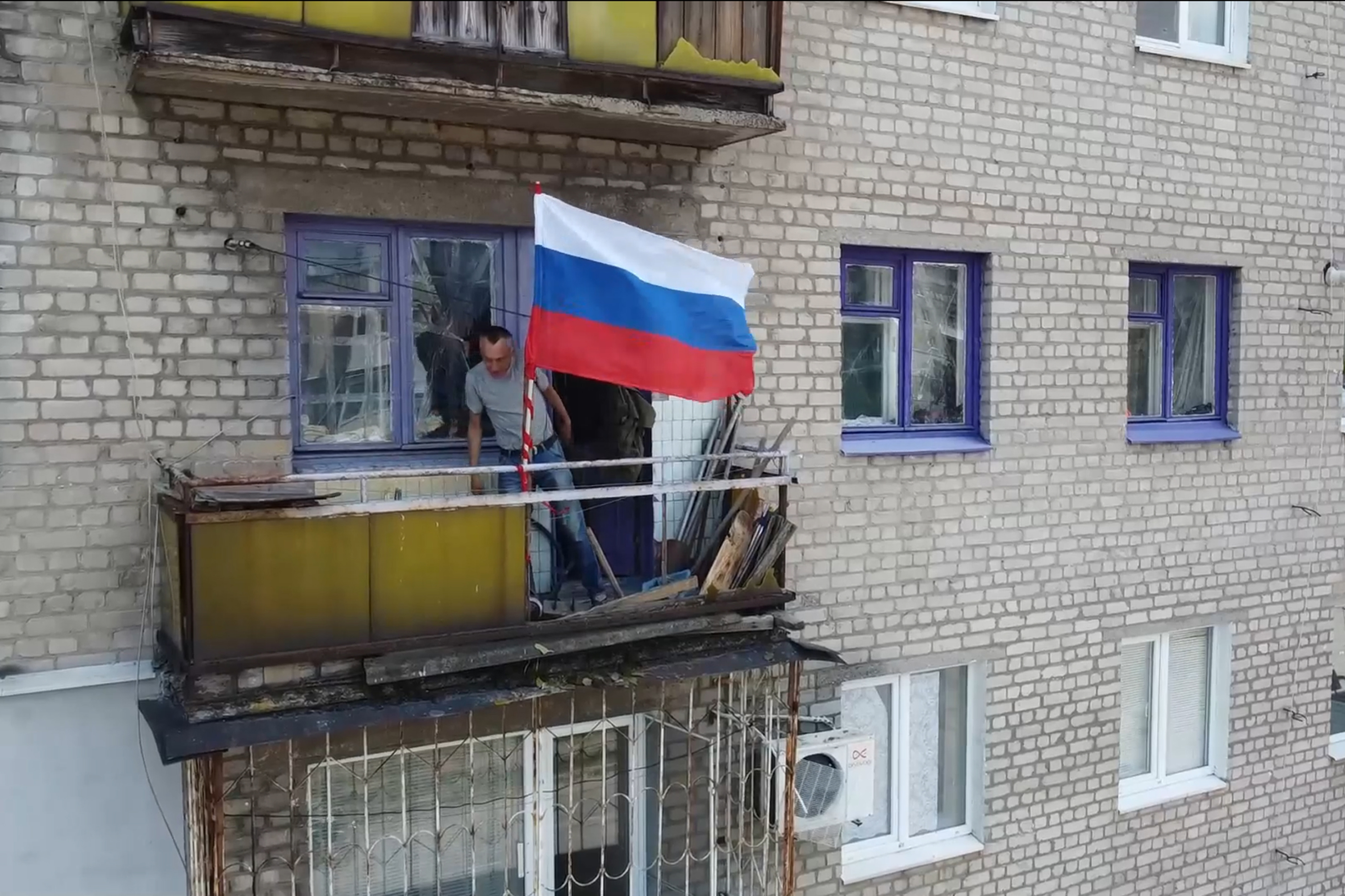 In this handout photo taken from video released by Russian Defense Ministry Press Service on Monday, July 4, 2022, A man sets a Russian national flag on a balcony of a residential building in Lysychansk, which is now territory under the Government of the Luhansk People's Republic control, eastern Ukraine. (Russian Defense Ministry Press Service via AP)