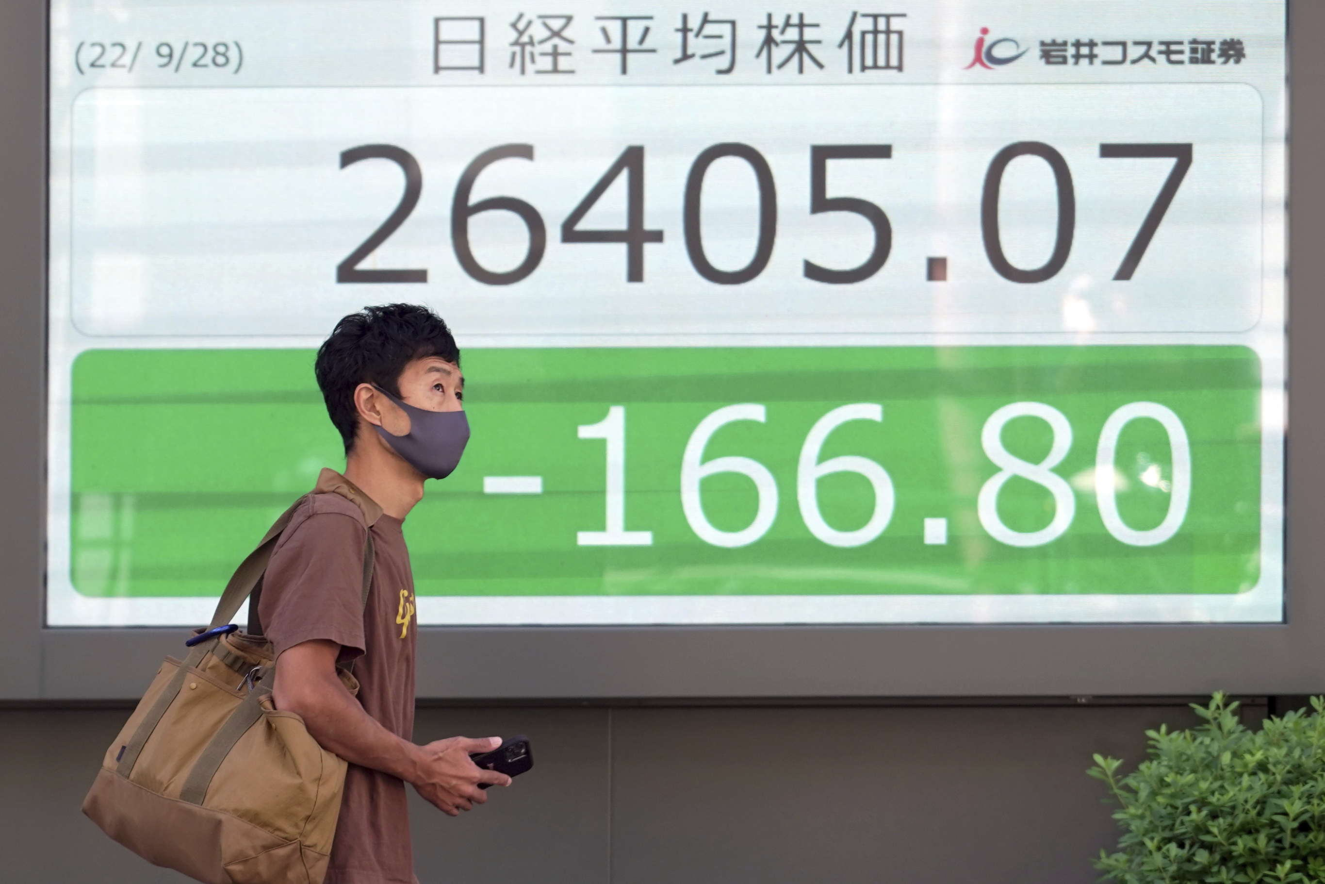 A person wearing a protective mask walks in front of an electronic stock board showing Japan's Nikkei 225 index at a securities firm Wednesday in Tokyo.