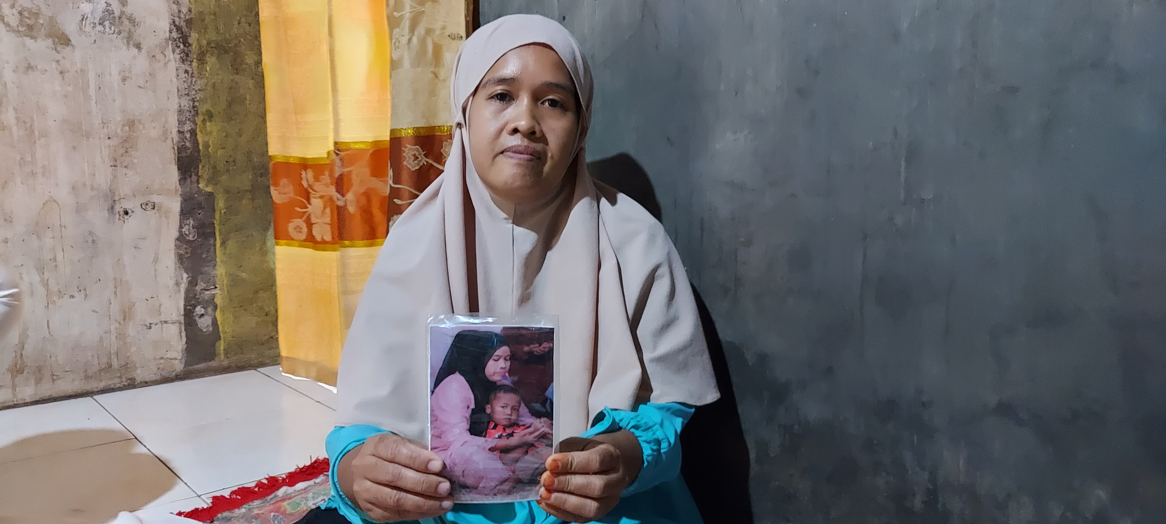 Siti sits in her house holding a picture showing her with her five year old son Mohammad Fajar