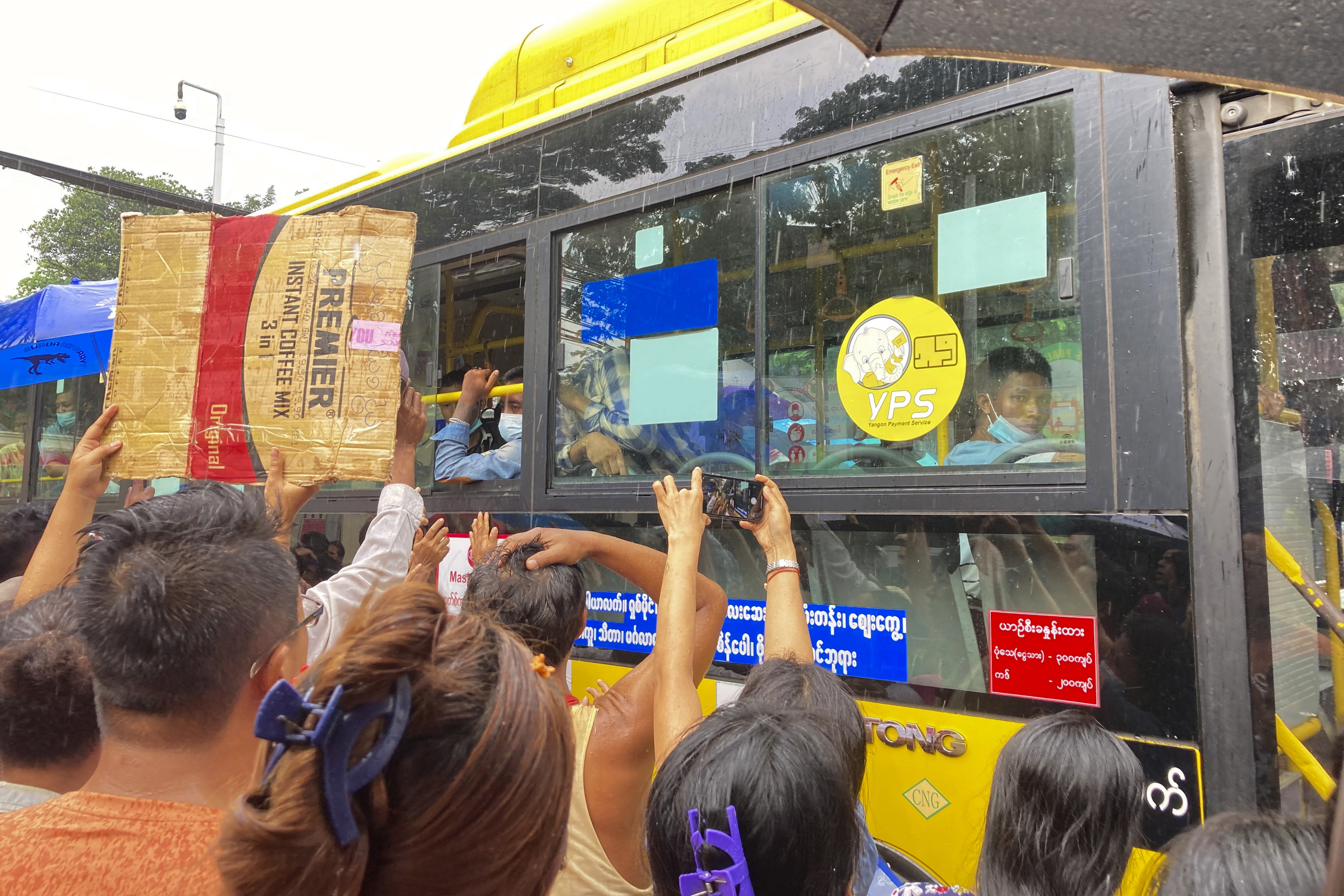 People stretching to reach the window of a bus, holding signs with names, as they hope their loved ones are released from prison