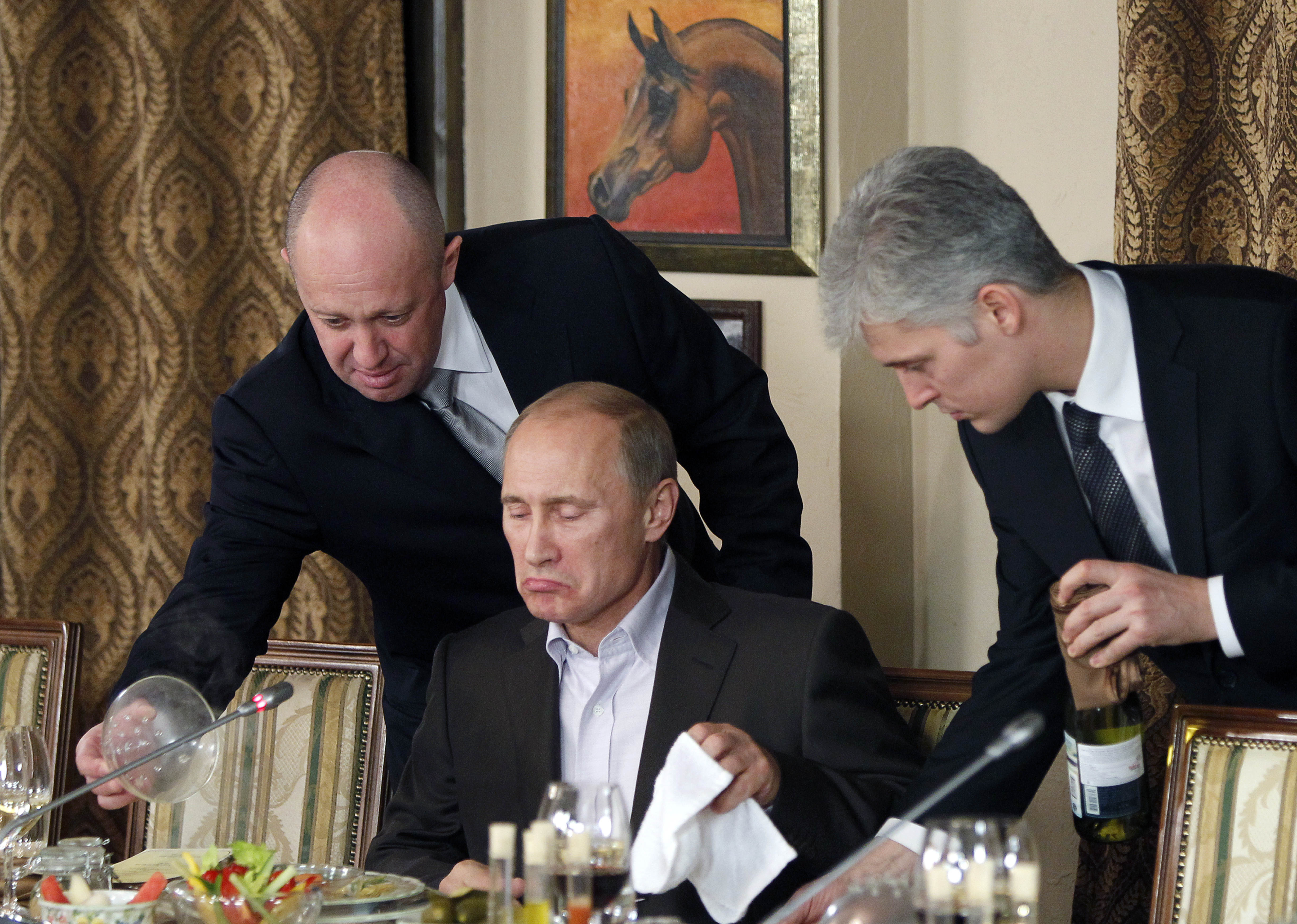 FILE - In this Friday, Nov. 11, 2011 file photo, businessman Yevgeny Prigozhin, left, serves food to Russian Prime Minister Vladimir Putin, center, during dinner at Prigozhin's restaurant outside Moscow, Russia. Russian news outlets say thousands of Russians have been deployed in Syria by a shadowy, private military contractor linked to Prigozhin. When President Vladimir Putin announced Monday Dec. 11, 2017 that Russia’s campaign in Syria was drawing to a close, he did not mention this secret force. (AP Photo/Misha Japaridze, Pool, File)