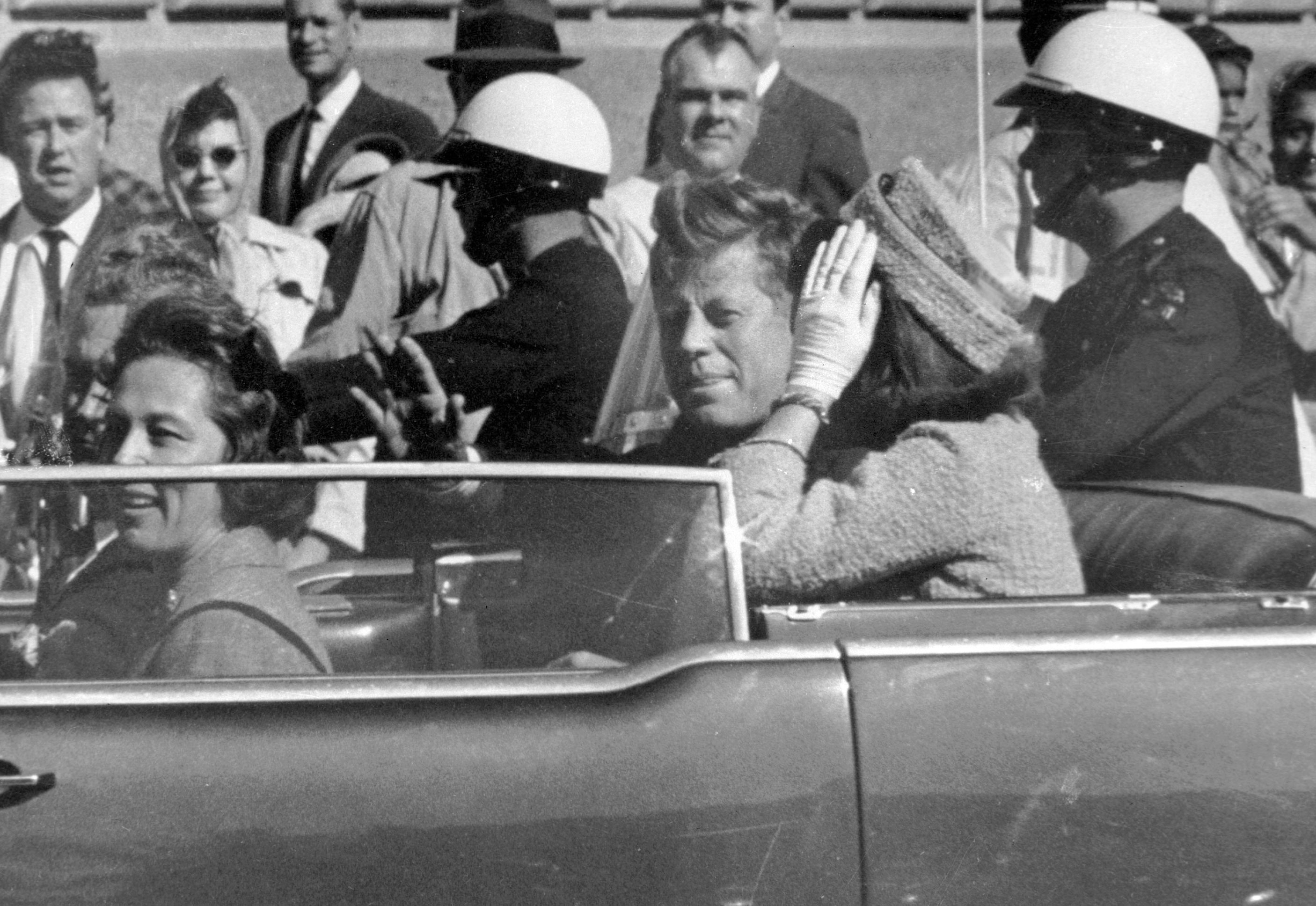 President John F Kennedy waves from his motorcade about one minute before he was shot in Dallas, Texas