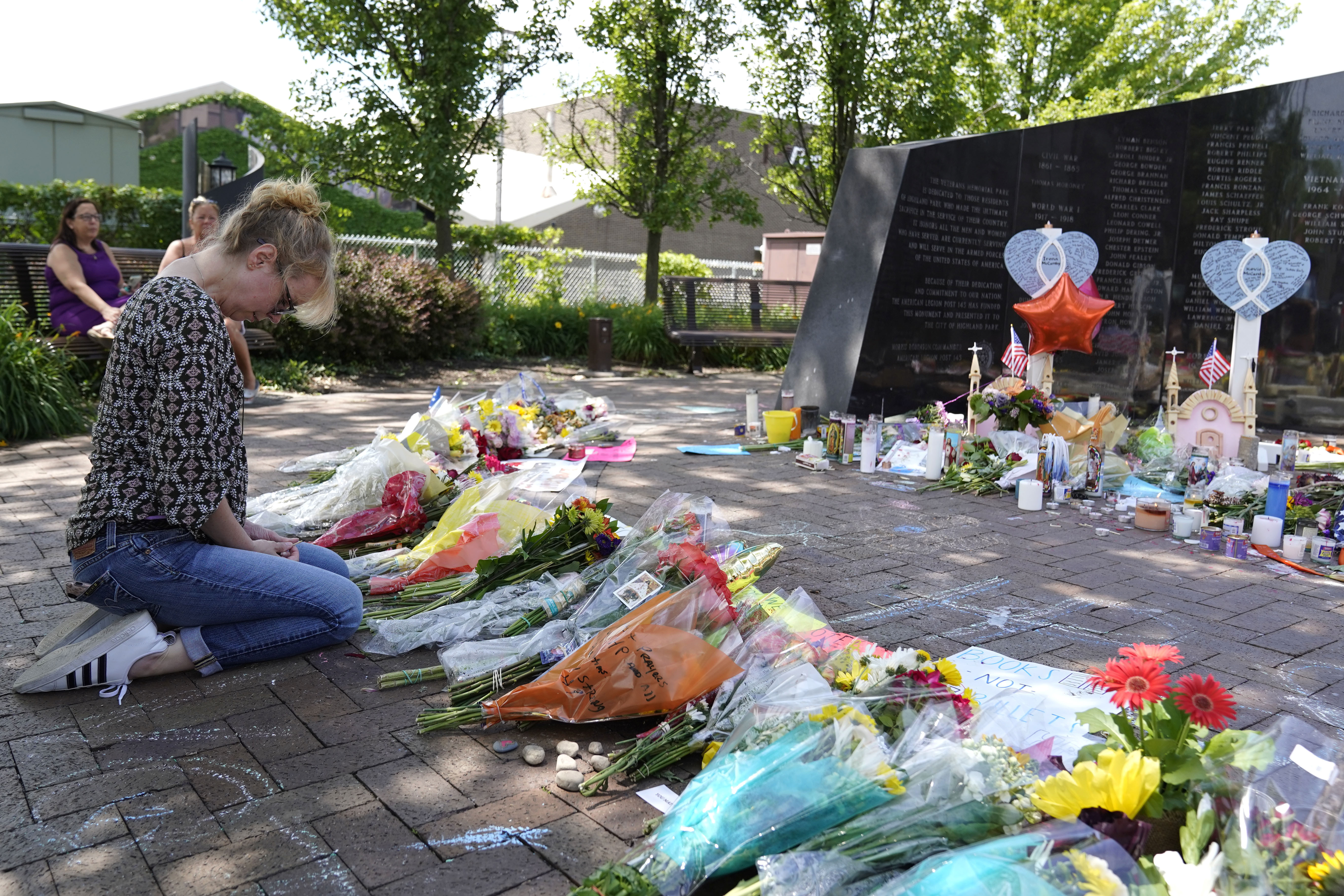A woman mourns in front of a memorial with bouquets