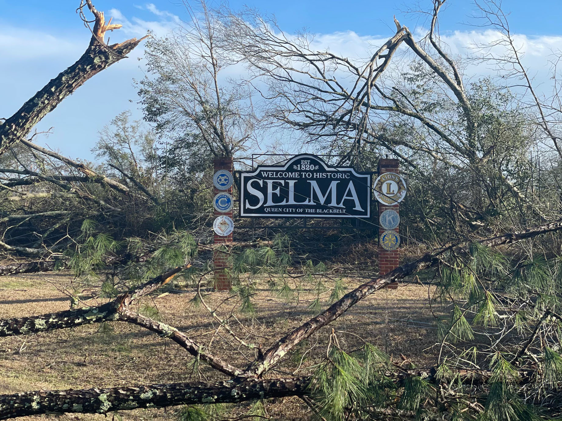 Fallen trees surround a sign welcoming visitors to Selma, Alabama
