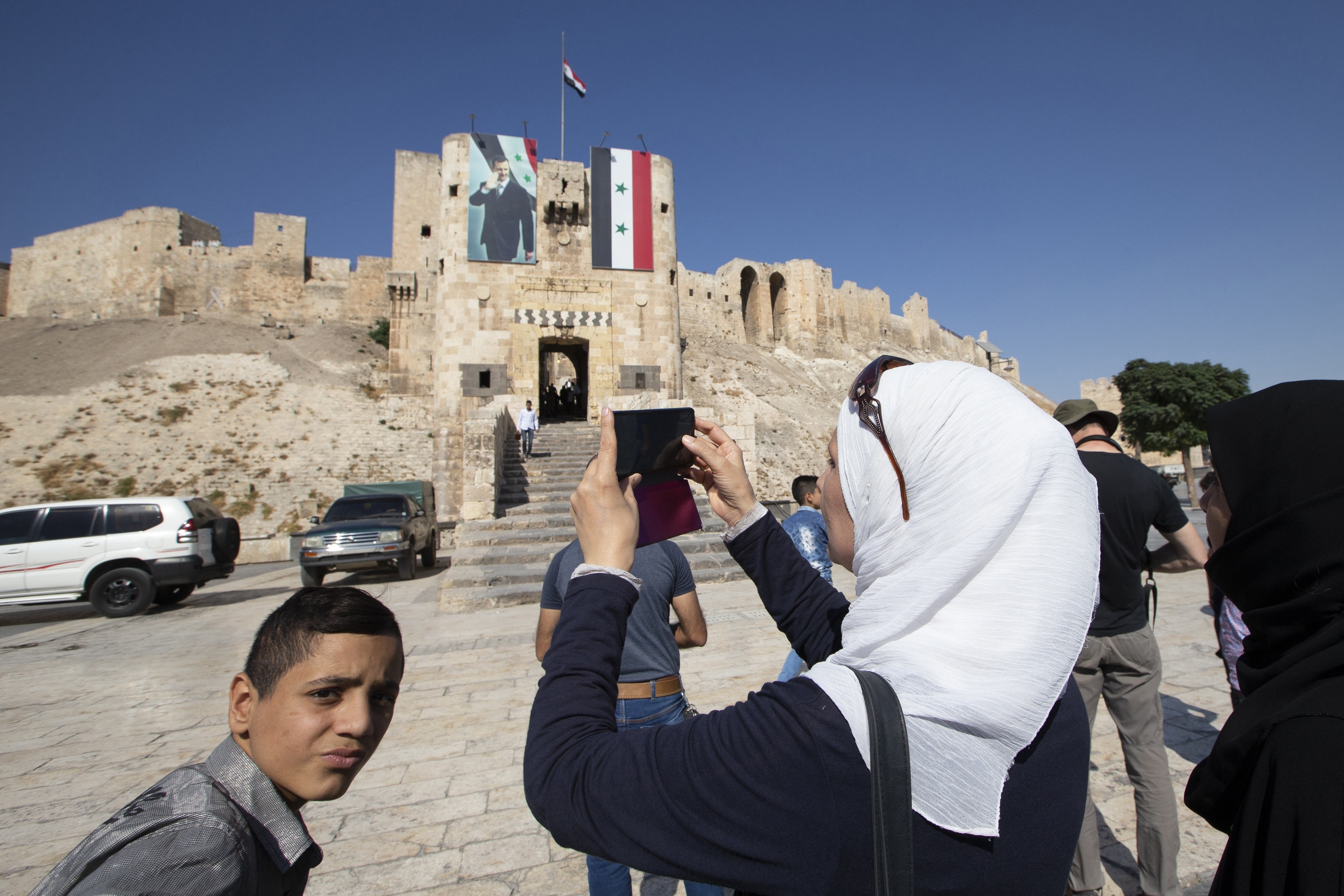 A Syrian woman takes a photo of the ancient Citadel, on the background, in Aleppo, Syria, Friday, Sept. 27, 2019. More than eight years of fighting has left many sections of Aleppo destroyed, and now authorities are pleading for international organisations to help fund restoration of the ancient city. (AP Photo/Alexander Zemlianichenko)