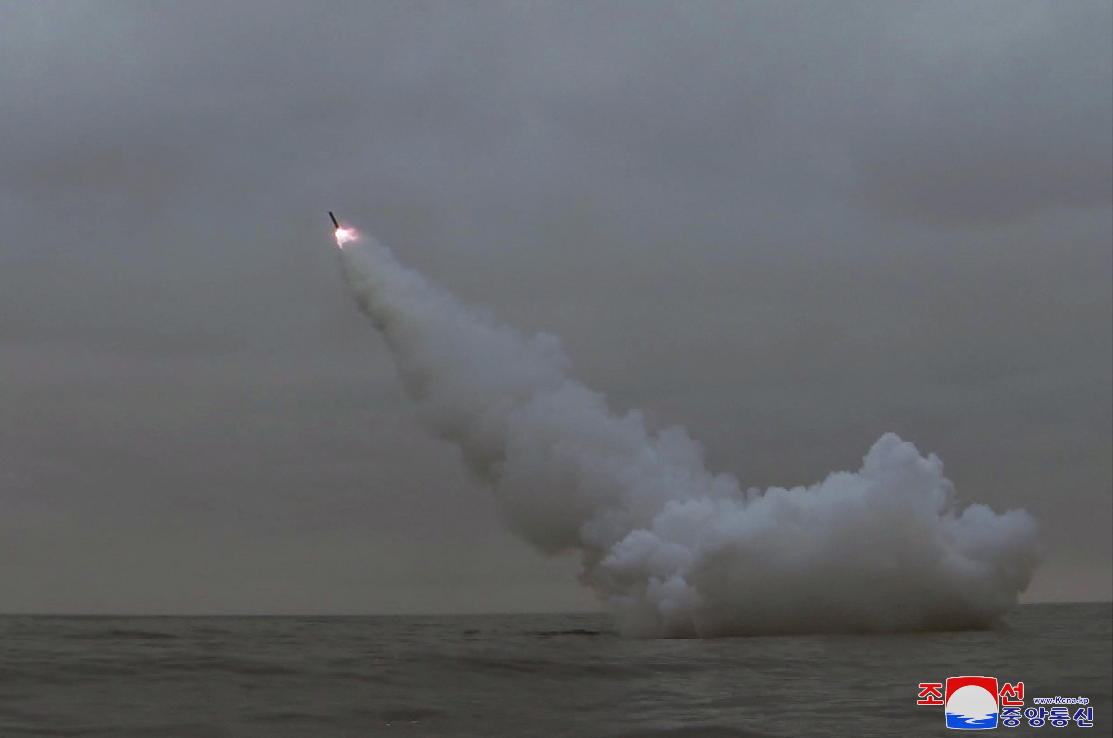 A weapon soaring into the air from the sea. Flames are visible at the tip and there is trail of white smoke clouds.