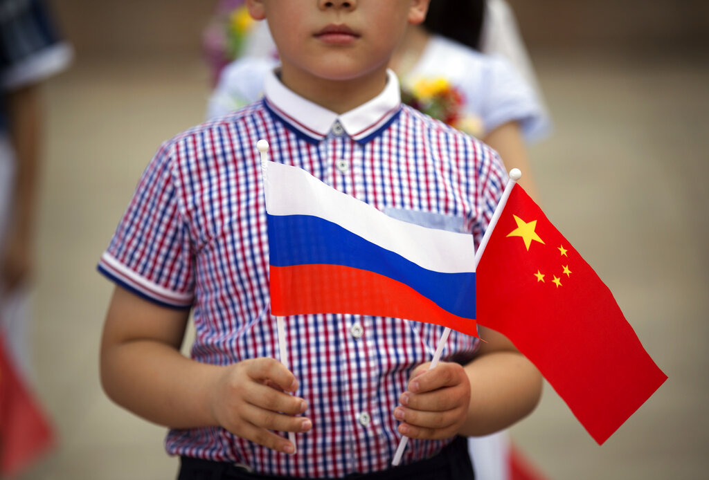 FILE - A boy holds Russian and Chinese flags before a welcoming ceremony for Russian President Vladimir Putin at the Great Hall of the People in Beijing on June 25, 2016. Three weeks ago, on the eve of the Beijing Winter Olympics, the leaders of China and Russia declared that the friendship between their countries "has no limits." But that was before Russia's invasion of Ukraine, a gambit that will test just how far China is willing to go. (AP Photo/Mark Schiefelbein, File)
