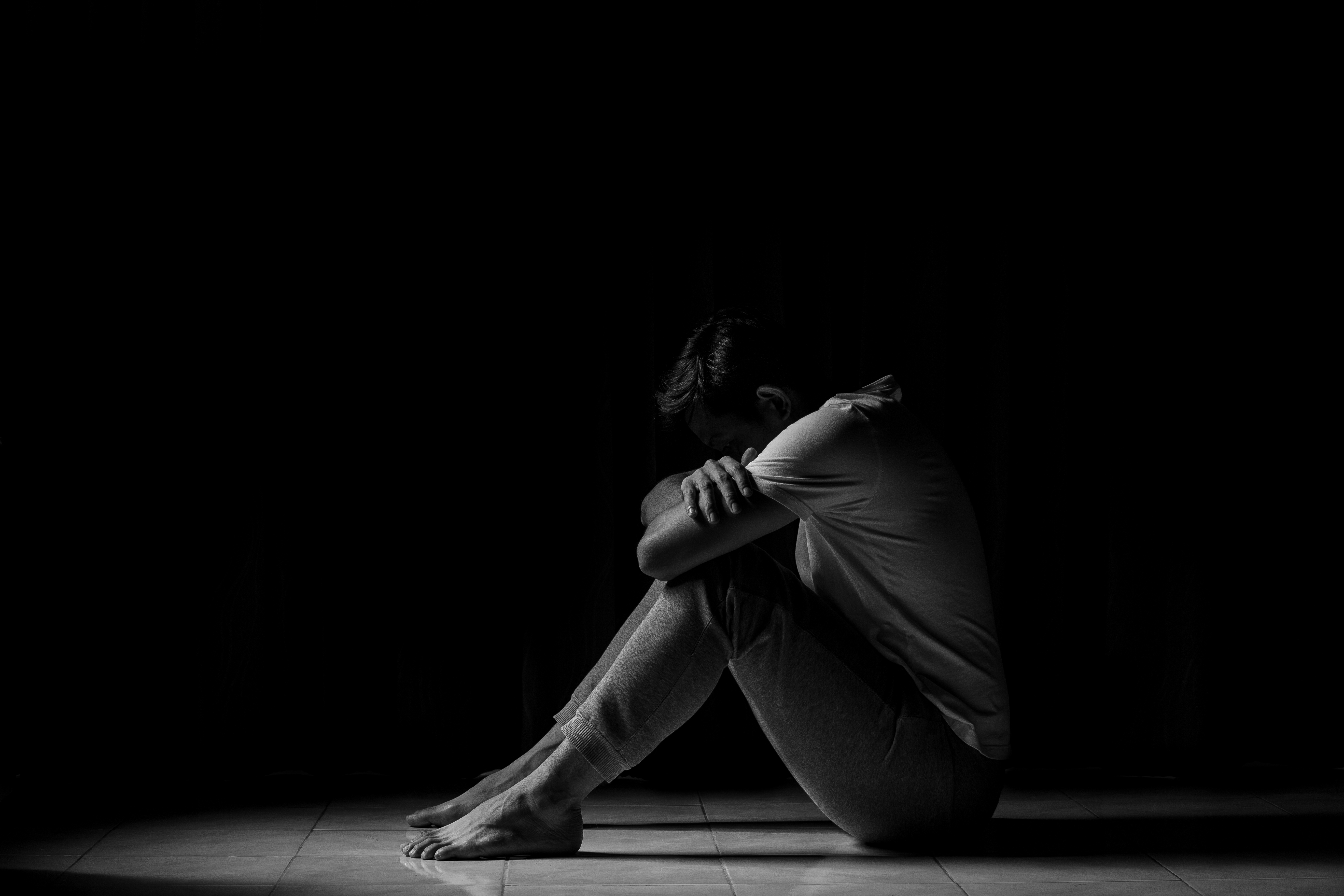 A man sits in a dark hallway with his head resting on his knees.