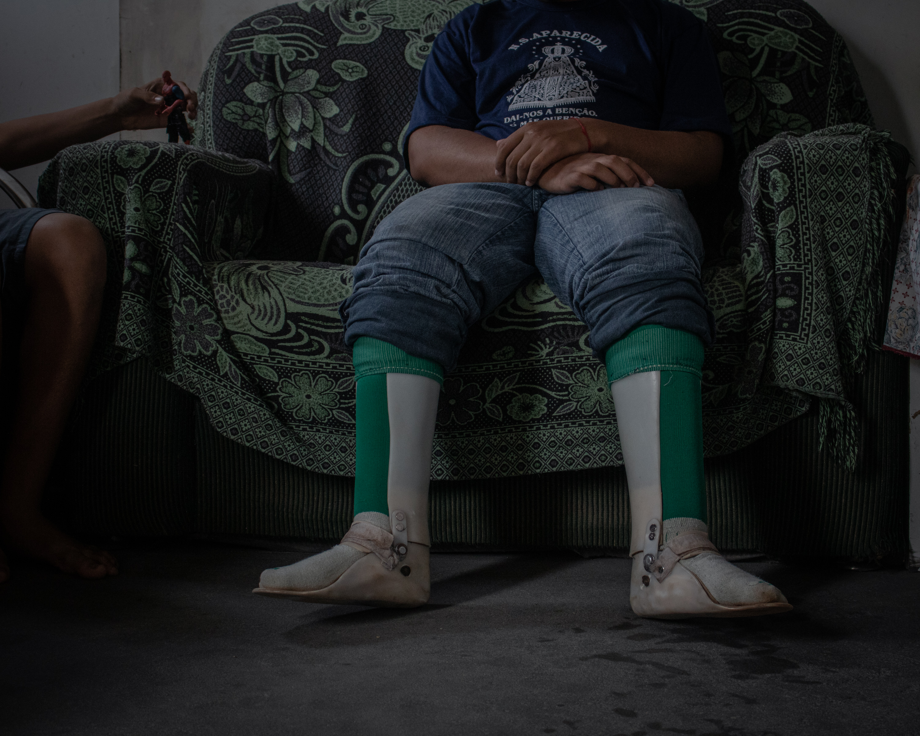 Cosme sits in the sofa, while Damião plays with a toy next to him