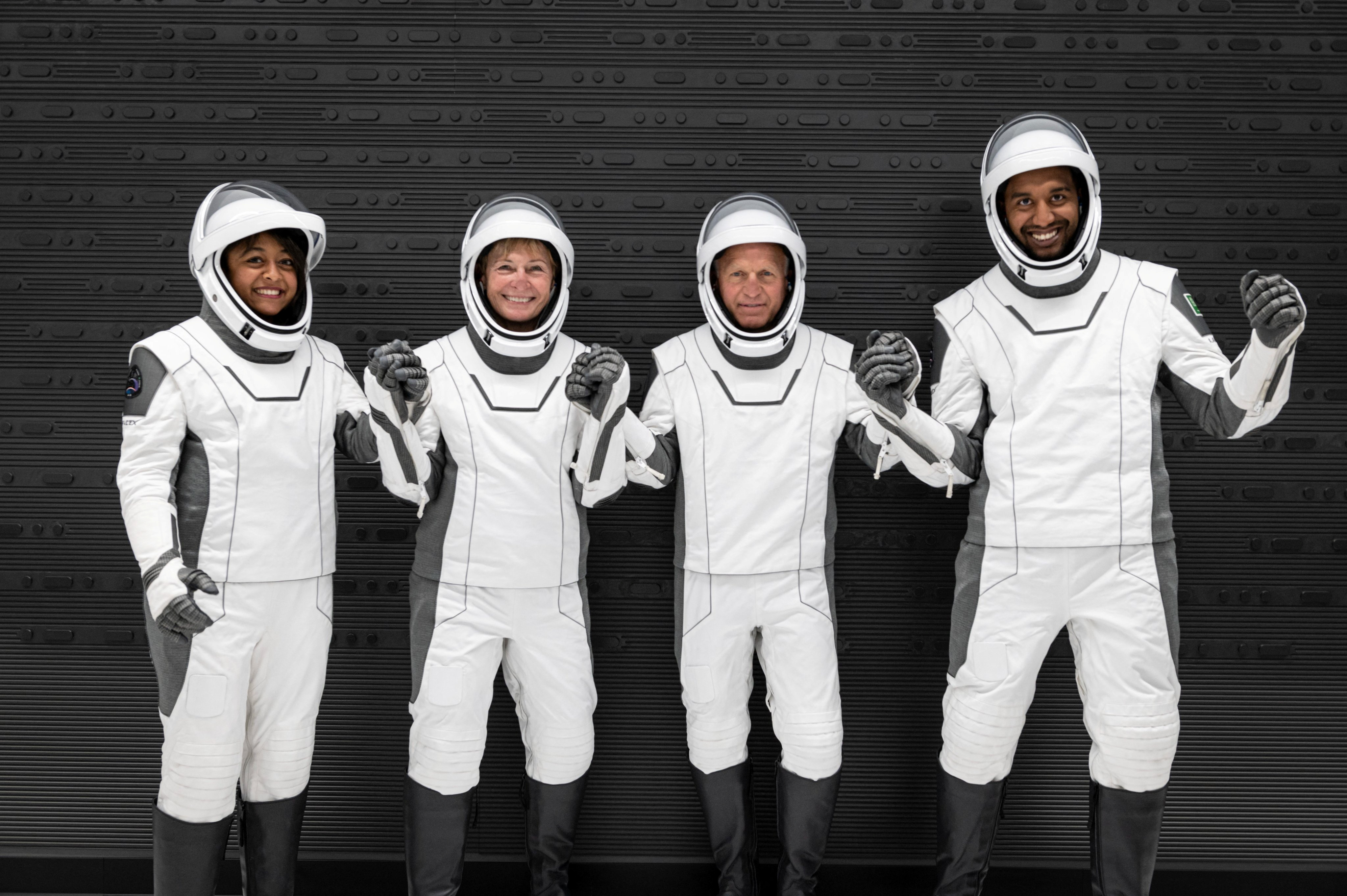 Saudi astronauts Rayyanah Barnawi and Ali Al Qarni, with their crew Peggy Whitson and John Shoffner pose for photos ahead of their mission to the International Space Station. They are wearing white spacesuits with black trim.