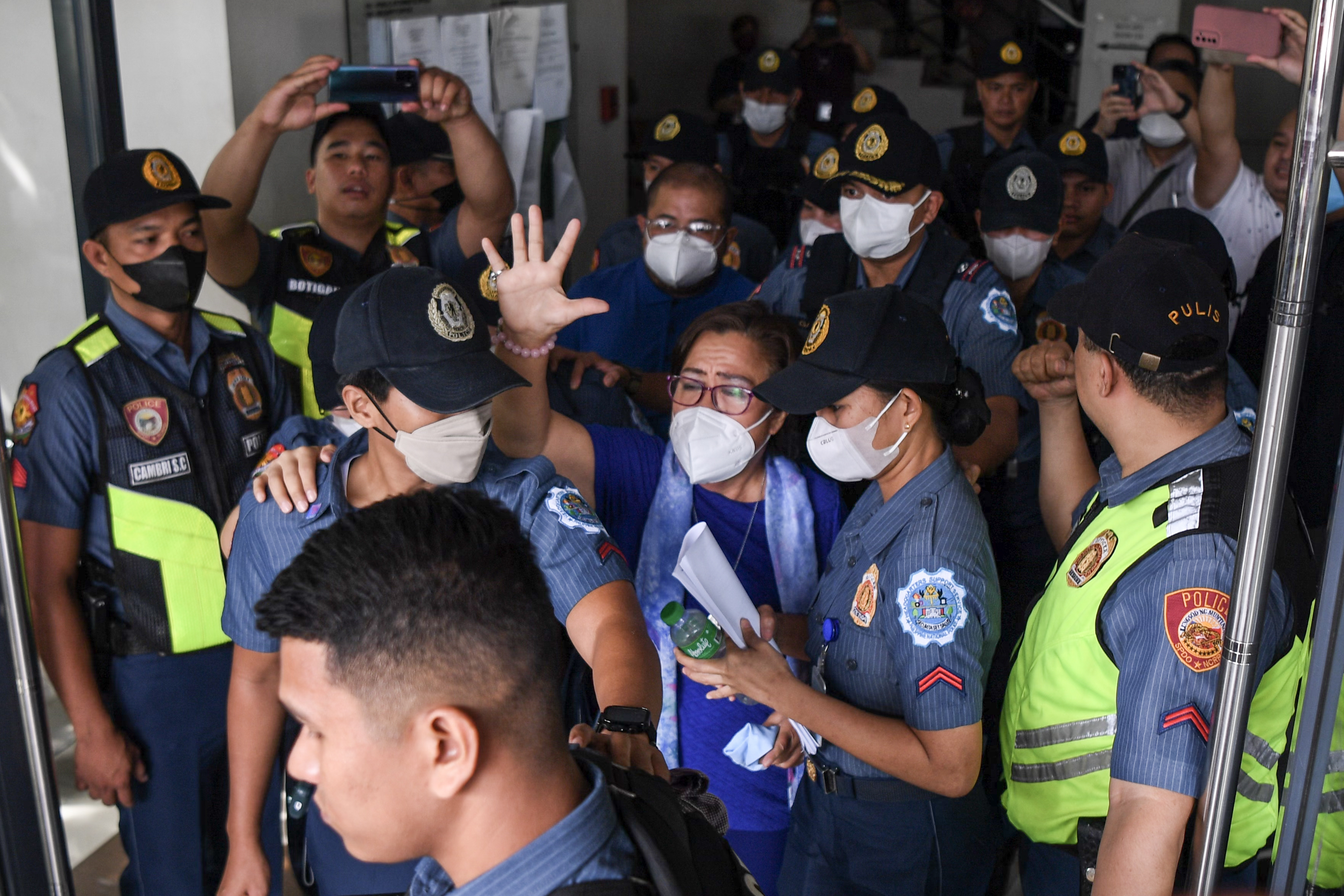 Leila de Lima waves as she's escorted from court. She is wearing a face mask and is surrounded by police.