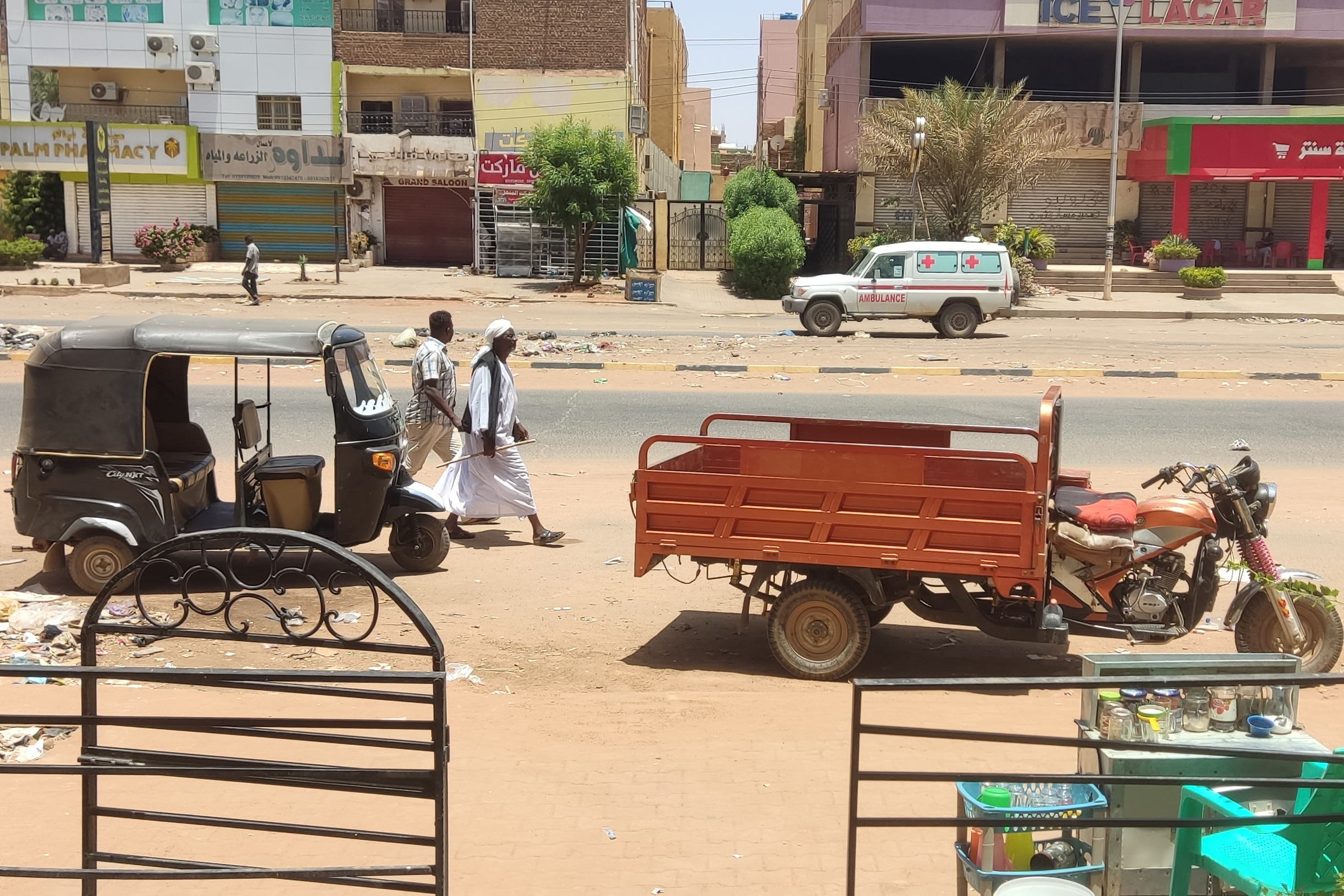 People walk past parked three-wheeled vehicles on al-Sittin Road in Khartoum, on May 22, 2023