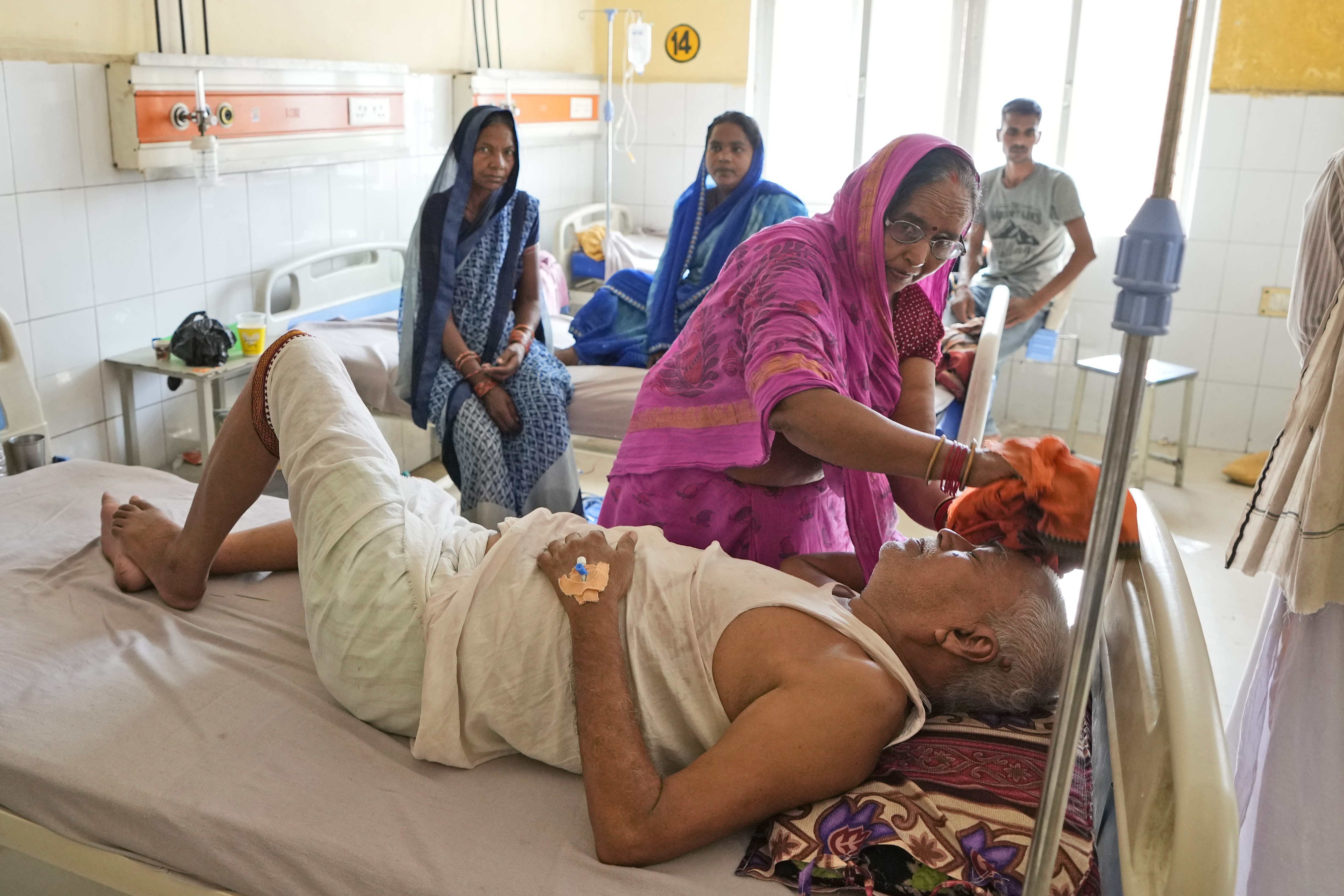 A woman wipes the head of her ailing brother using a wet cloth at a hospital in Ballia