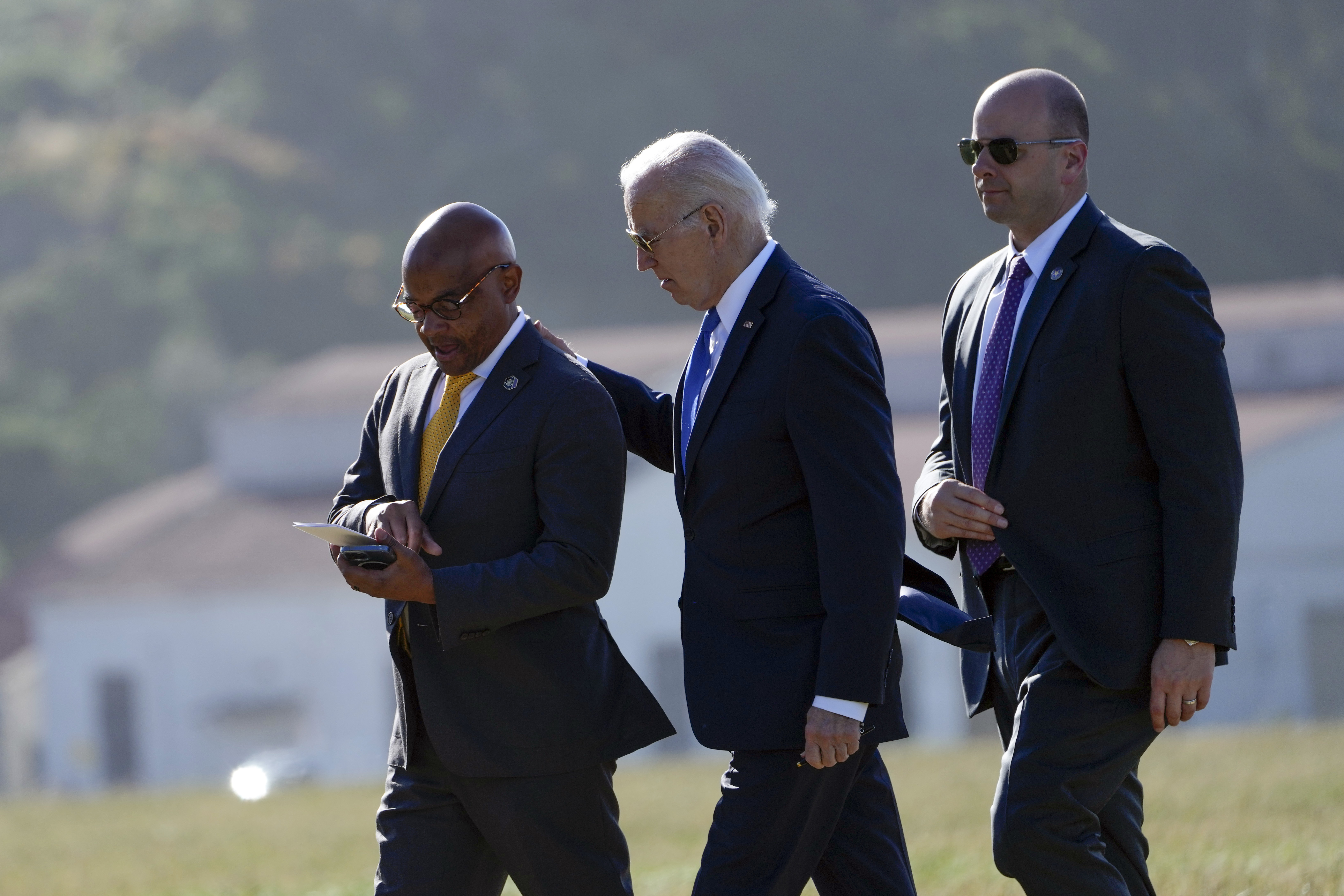 Joe Biden walking with an aide. He is patting the aide on the shoulder. Biden is wearing his trademark aviator-style sunglasses.