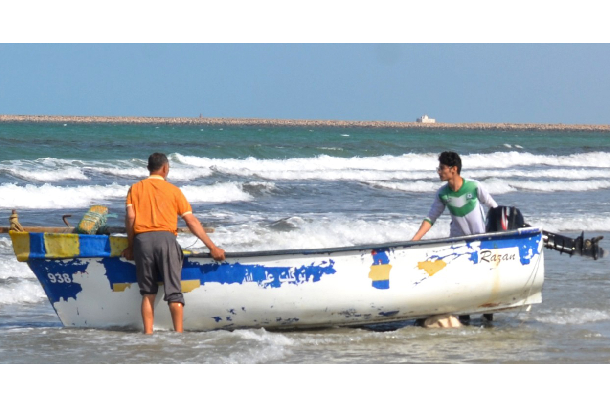 Two men launch a boat into the sea