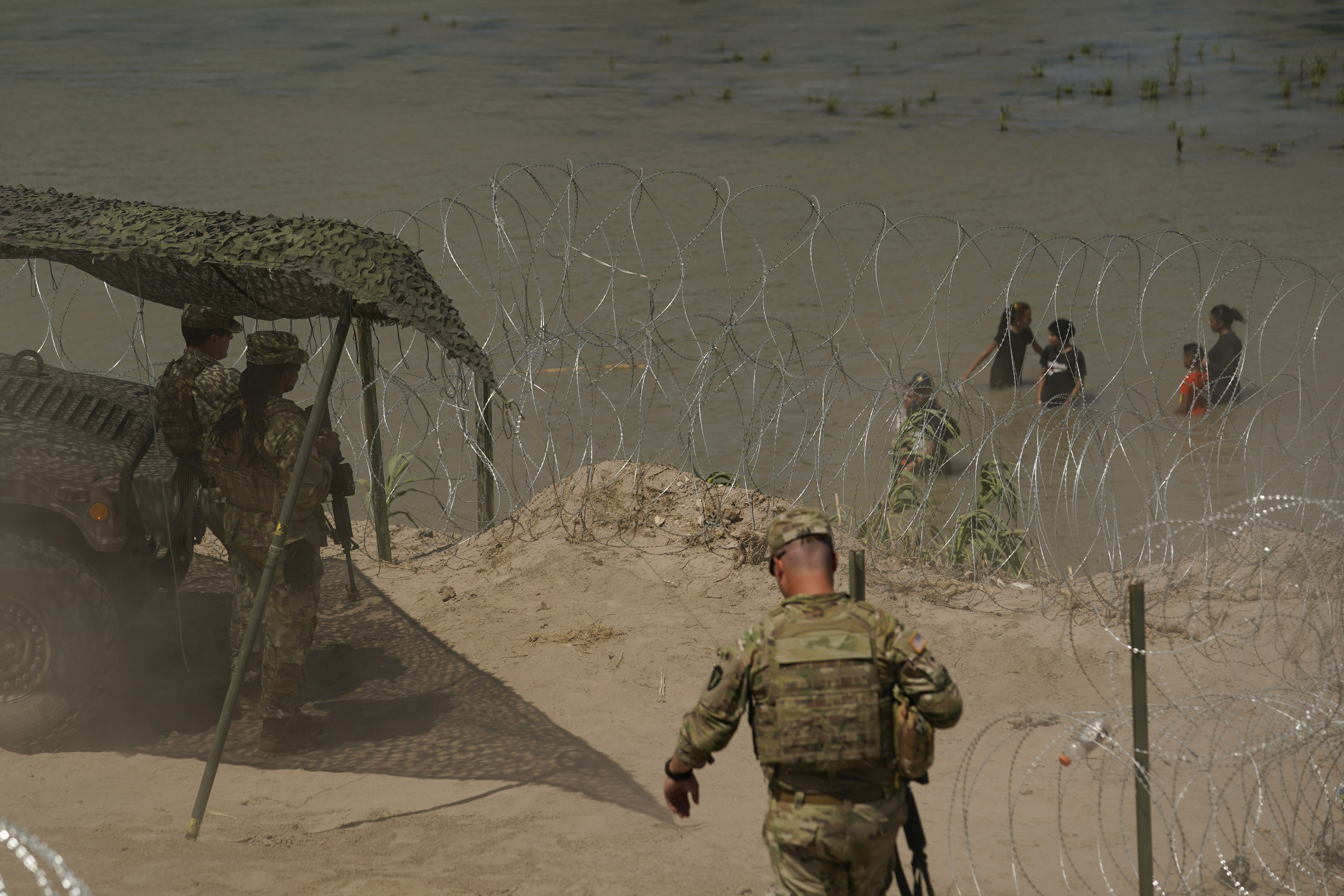 Guardsmen watch as migrants try to cross the Rio Grande