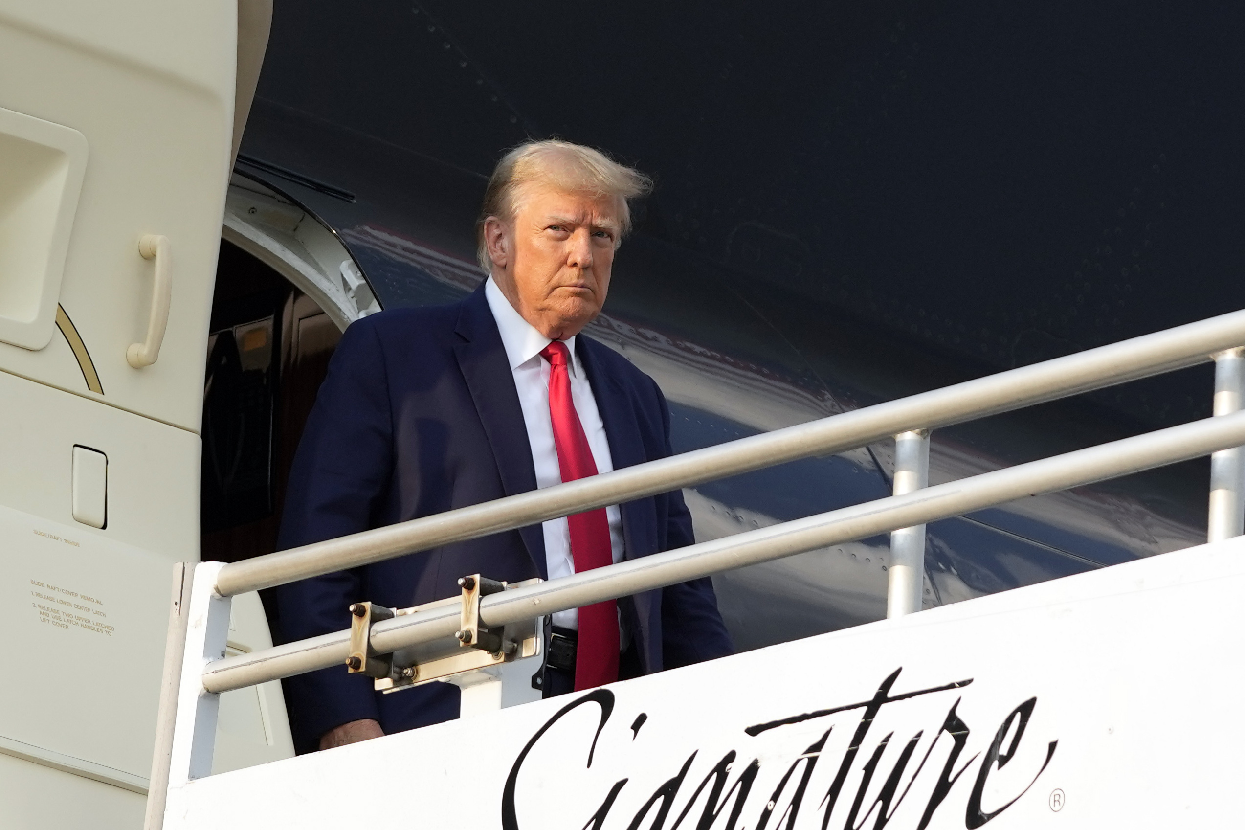 Trump getting of his plane as he arrives in Atlanta. He's in a blue suit with red tie.
