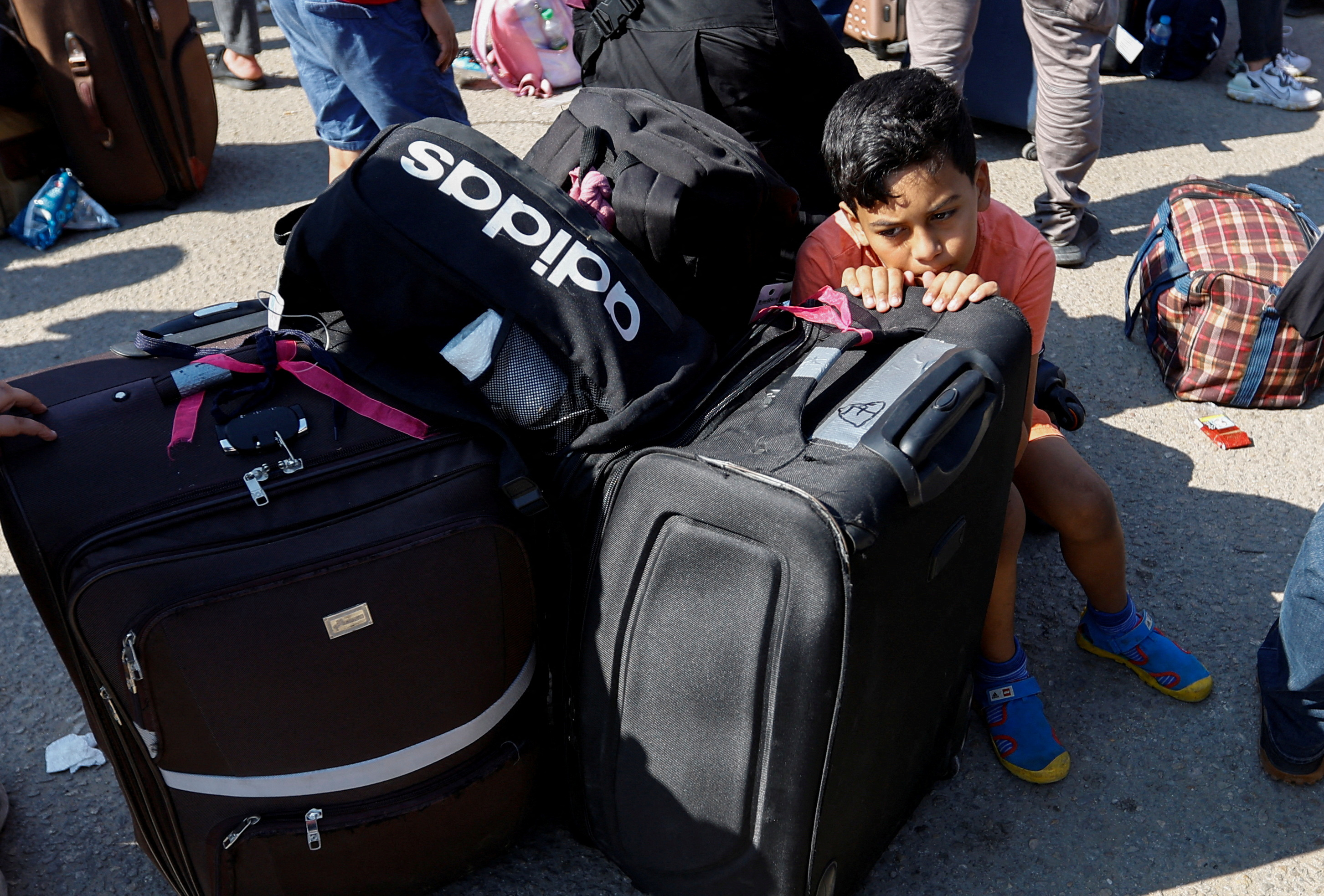 A small child seemingly cowers behind a black suitcase as his family waits along the southern Gaza border.