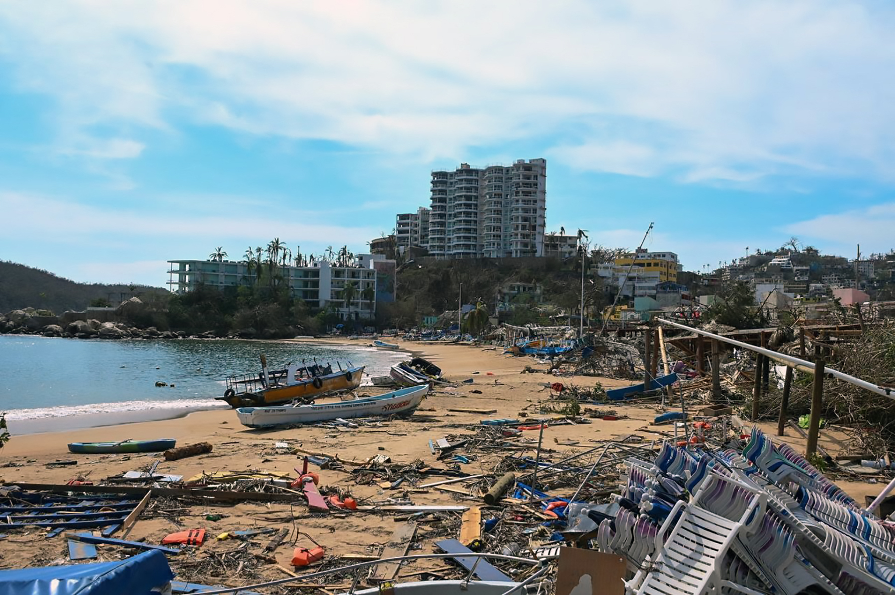 Debris across a beach in Acupulco with damaged buildings behind