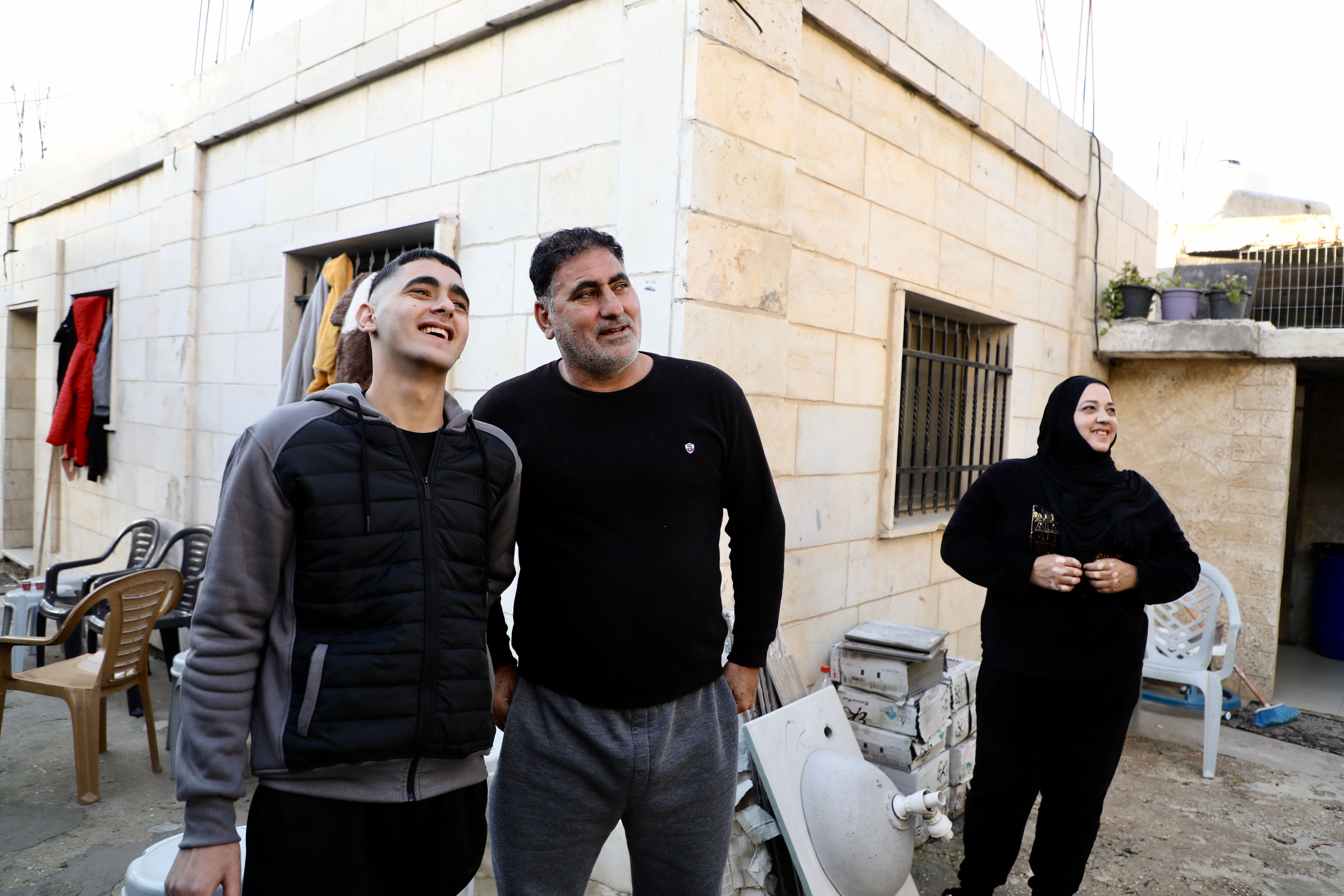 Ubai and his parents outside their modest home, smiles all around