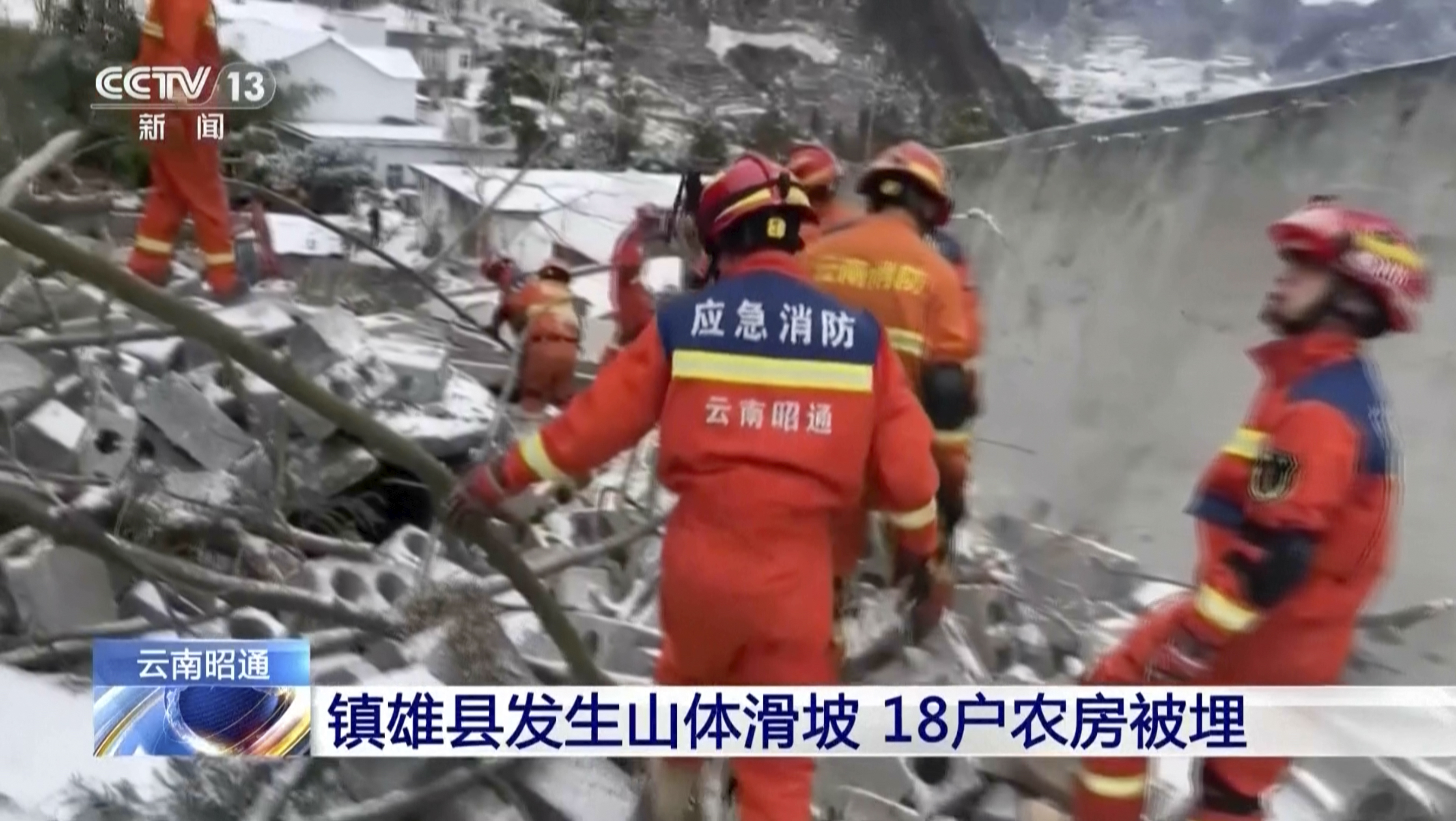 Rescuers at the landslide location. They are in orange uniforms with hard hats. There is a ticker at the bottom because the picture has been taken from a TV broadcast