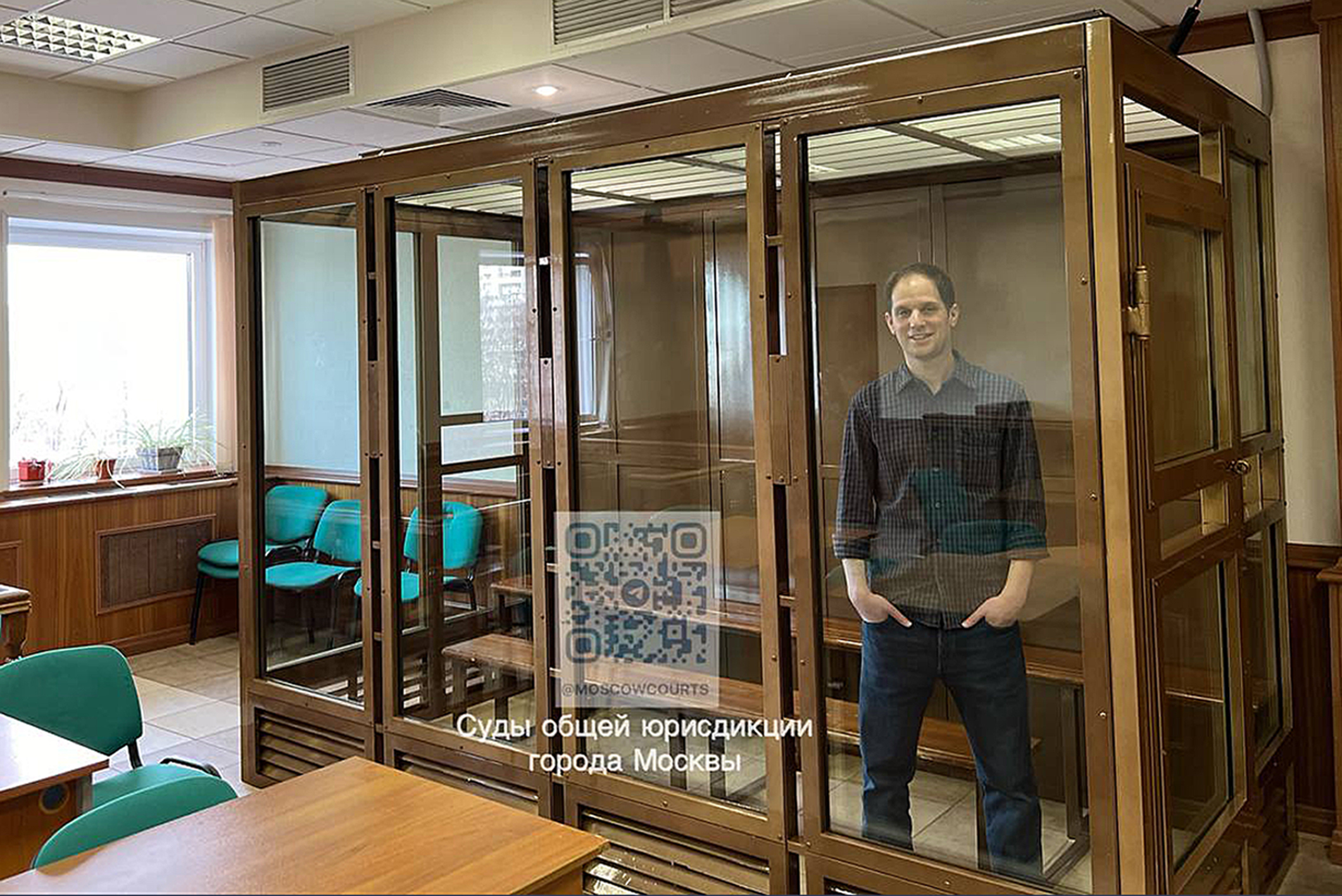 Reporter Evan Gershkovich stands in a glass cage in a courtroom