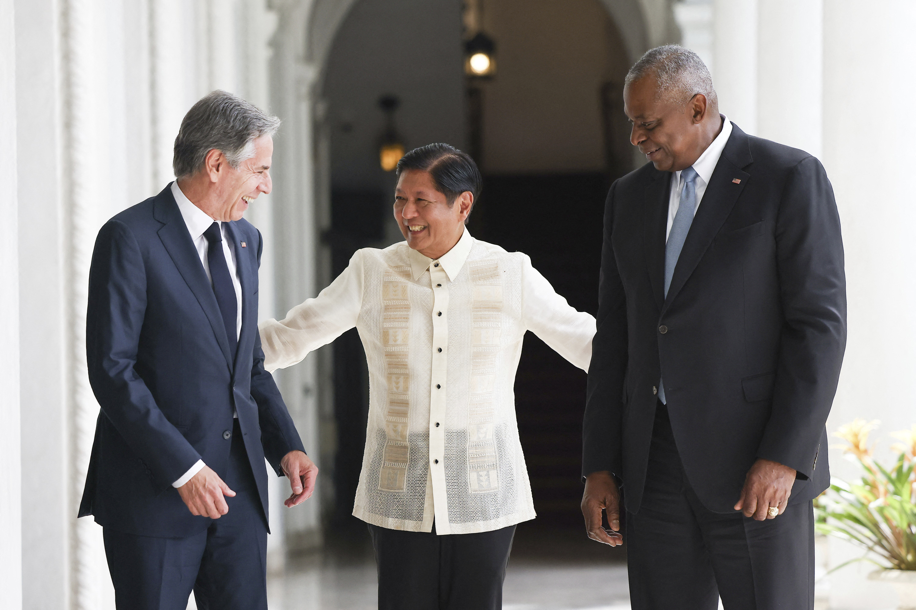 Ferdinand Marcos Jr with Antony Blinken and Lloyd Austin. They are in the Malacanang Palace in Manila. Marcos Jr is wearing a traditional cream-coloured Filipino shirt. Blinken and Austin are in dark suits. They are laughing and smiling.