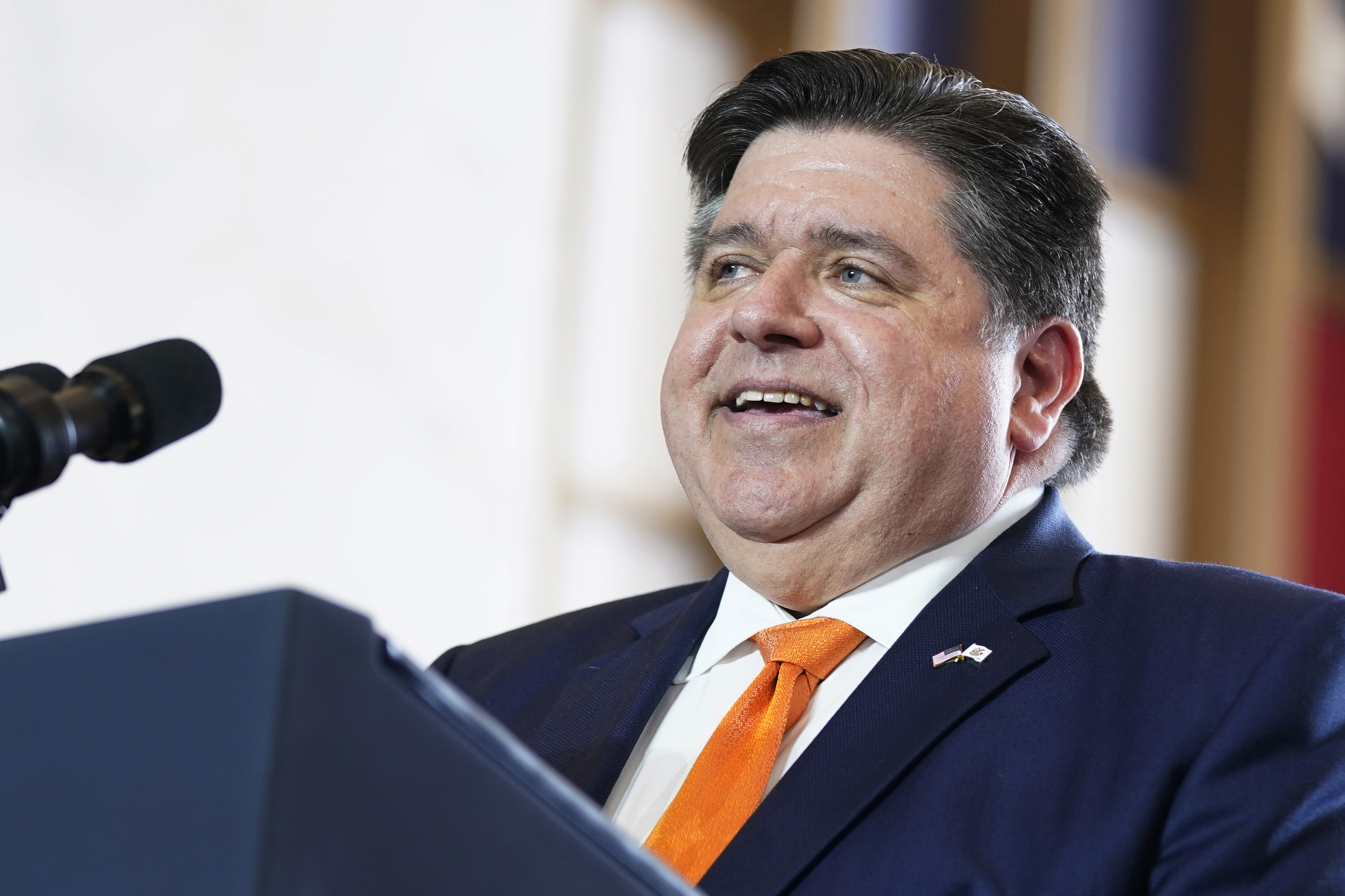 JB Pritzker speaking at a podium in suit and tie.