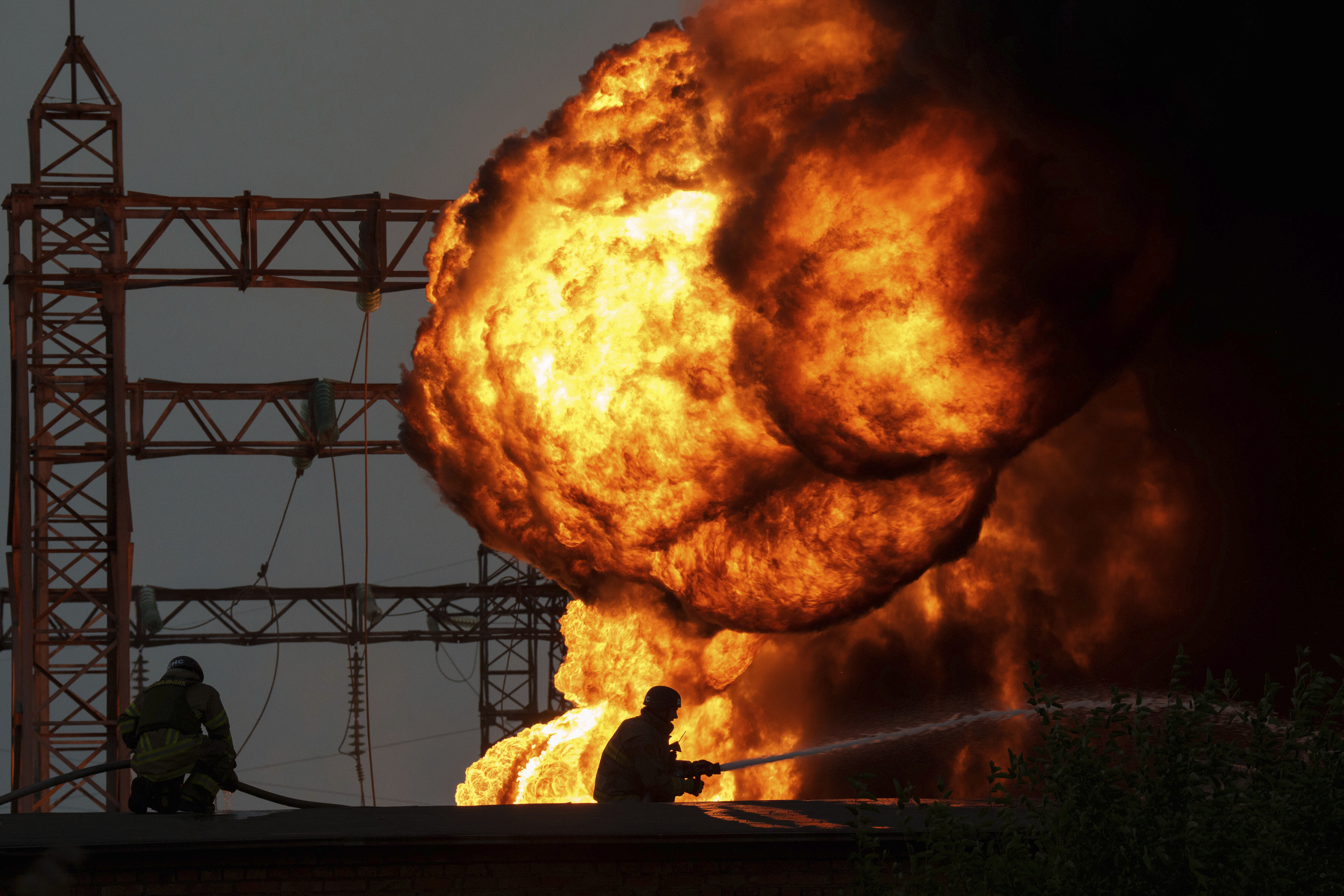A ball of orange flame rising into the air. Firefighters are silhouetted in front trying to put out the fire