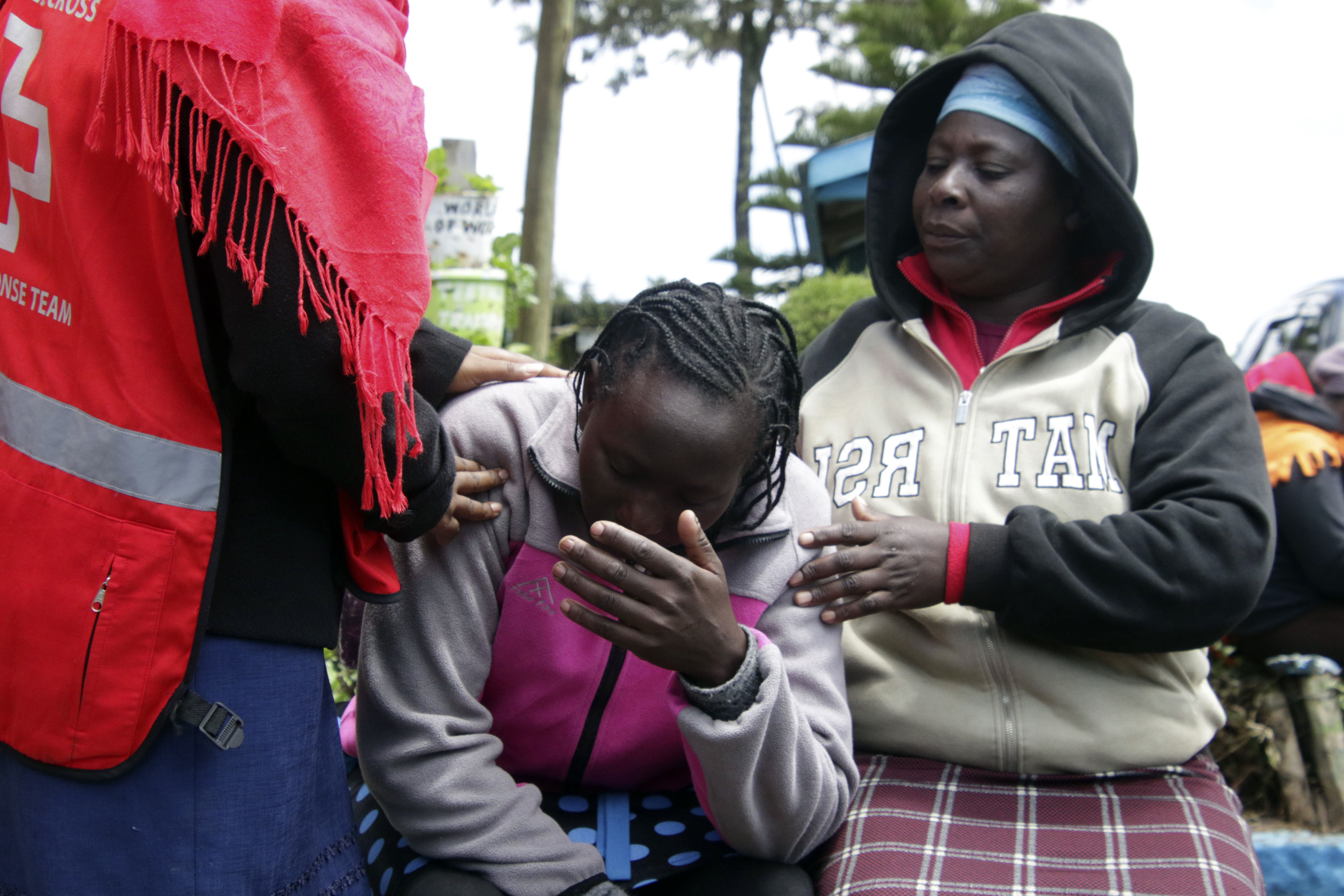 Kenya Red Cross personnel and relatives try to comfort a woman reacting near a burned-out dormitory