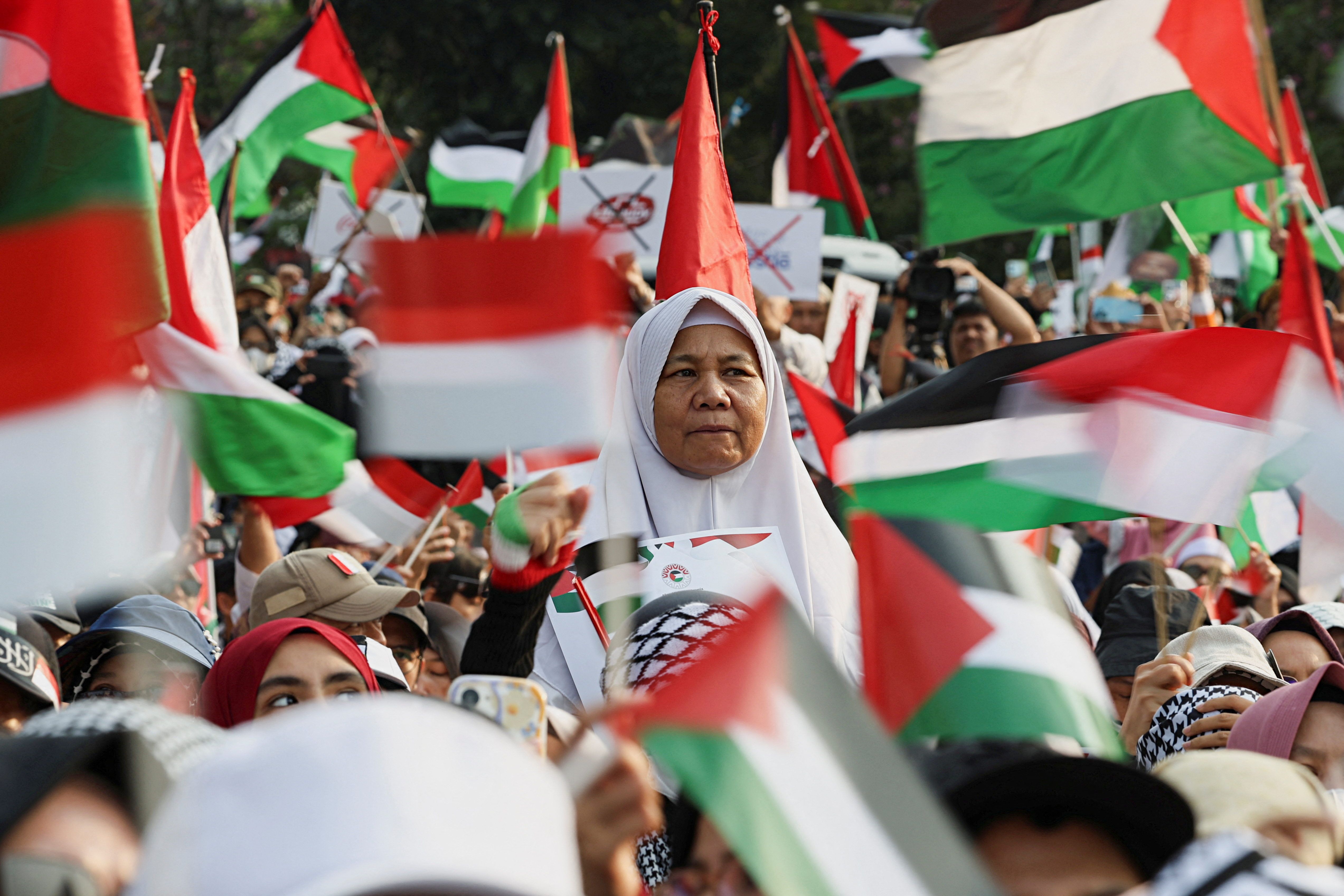 A woman looks on while people raise Palestinian flags during a protest against Israel and in support of Palestinians outside the U.S. embassy in Jakarta, Indonesia, October 6, 2024.