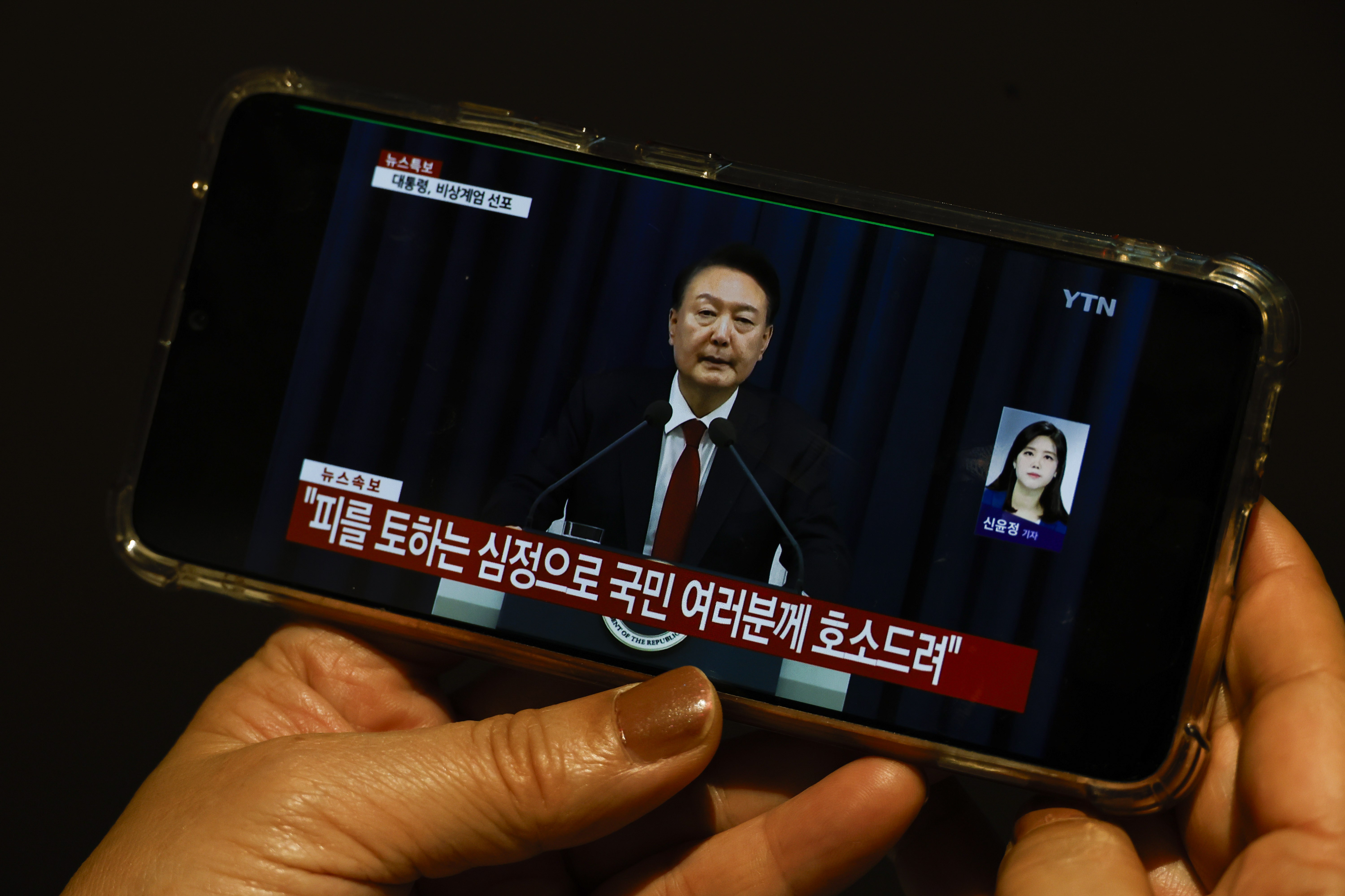 A South Korean tourist watches a Japanese TV broadcast on a phone showing Yoon declaring martial law in a televised emergency address