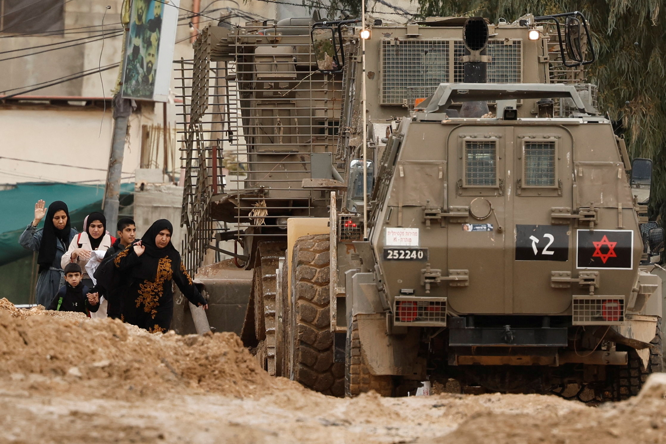 Palestinians walk next to heavy machinery and armored vehicles on a damaged street as they leave Jenin camp during an Israeli raid, in the Israeli-occupied West Bank, January 22, 2025. REUTERS/Raneen Sawafta
