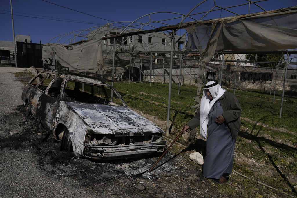 A Palestinian stands beside a torched car in the aftermath of an attack by suspected Israeli settlers in the West Bank village of Jinsafut on January 21, 2025