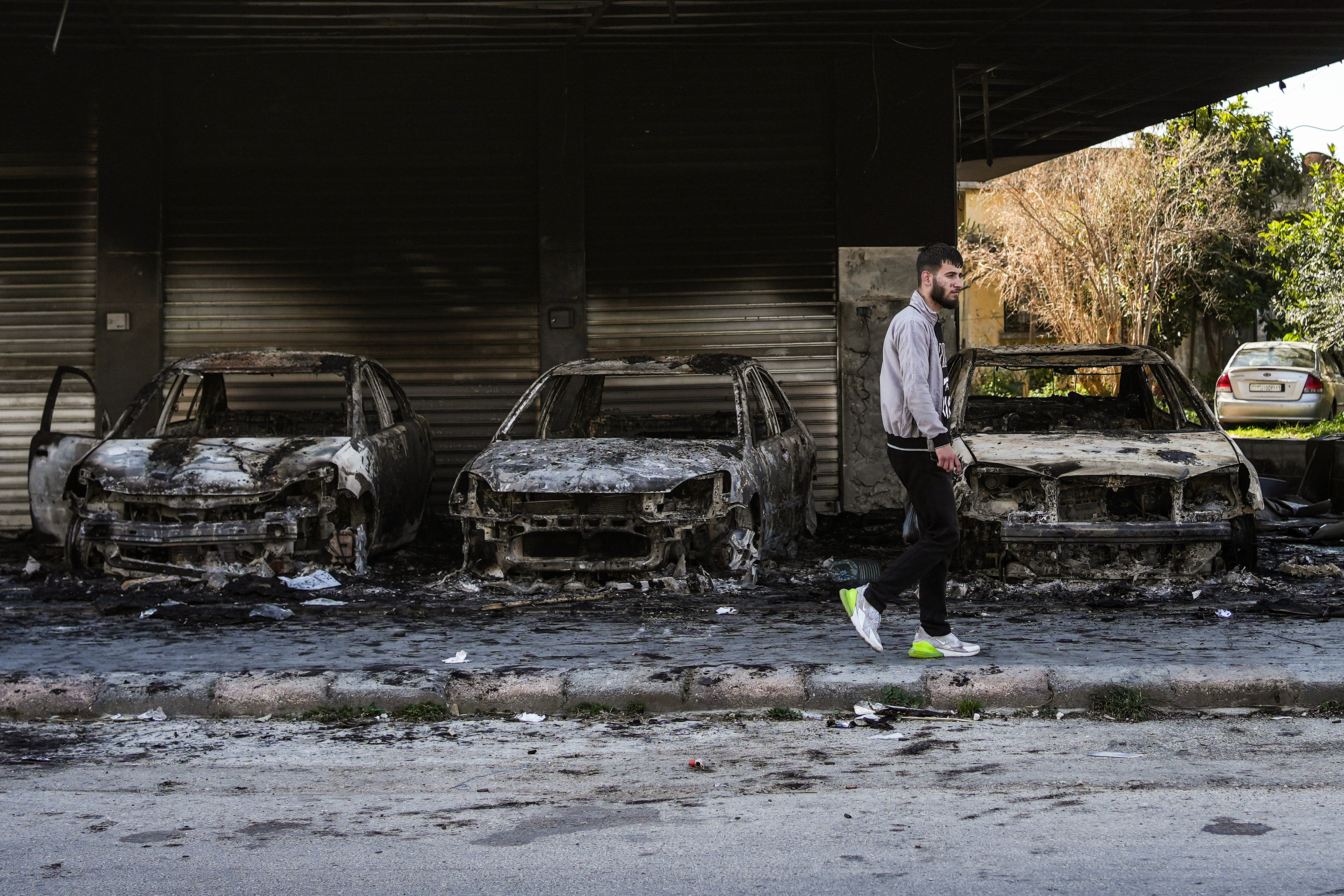 A man walks past burned-out cars in Jableh, 25km south of Latakia, following violence between Syrian security forces and armed fighters loyal to al-Assad on Syria’s coast, on March 20, 2025