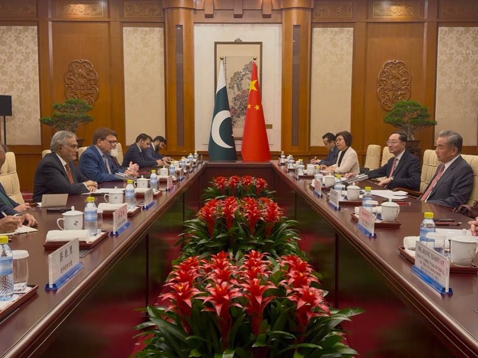 Officials sitting in meeting room with the Pakistan and China flags in the background.