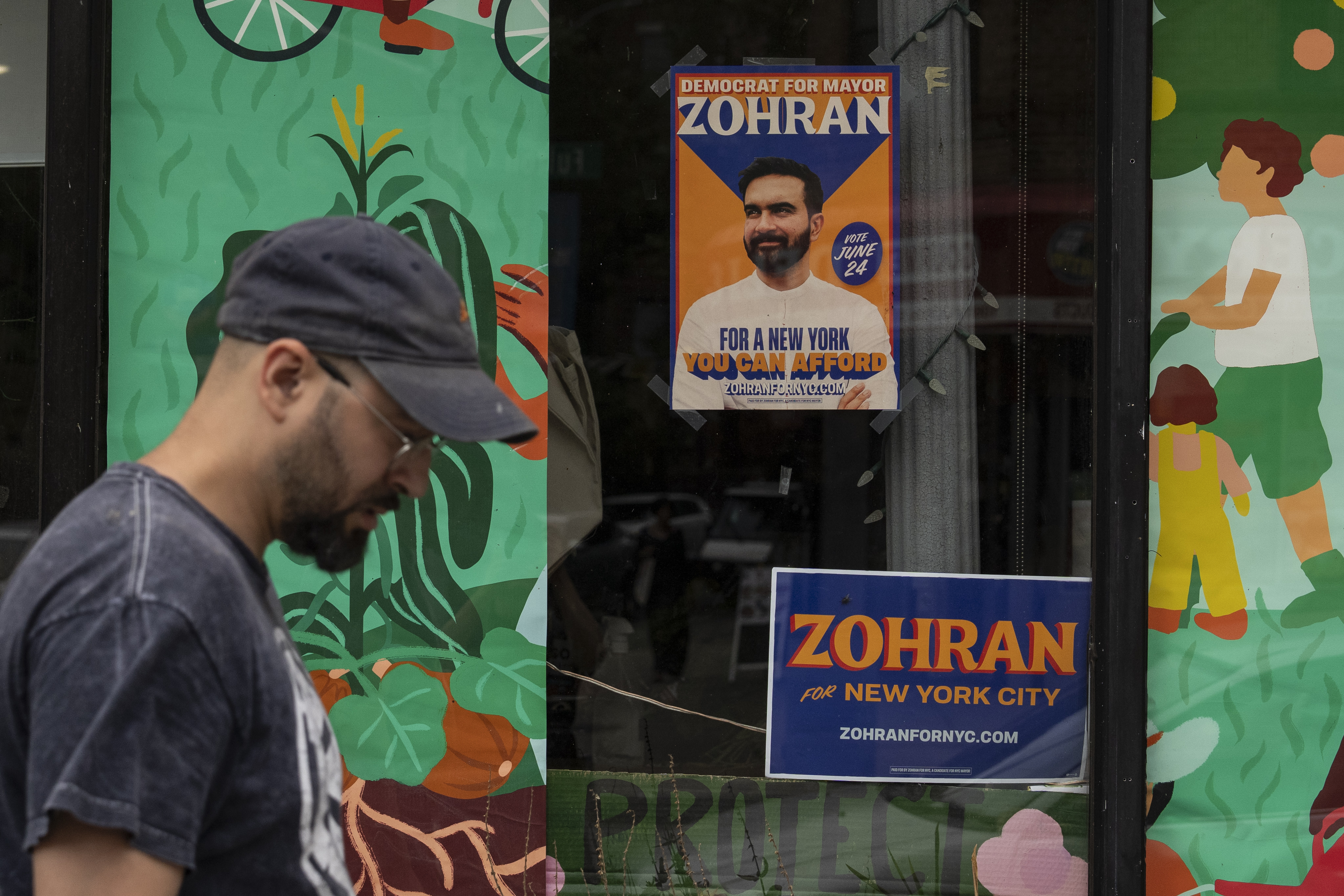 A pedestrian walks past two signs advertising Zohran Mamdani’s mayoral bid on June 26