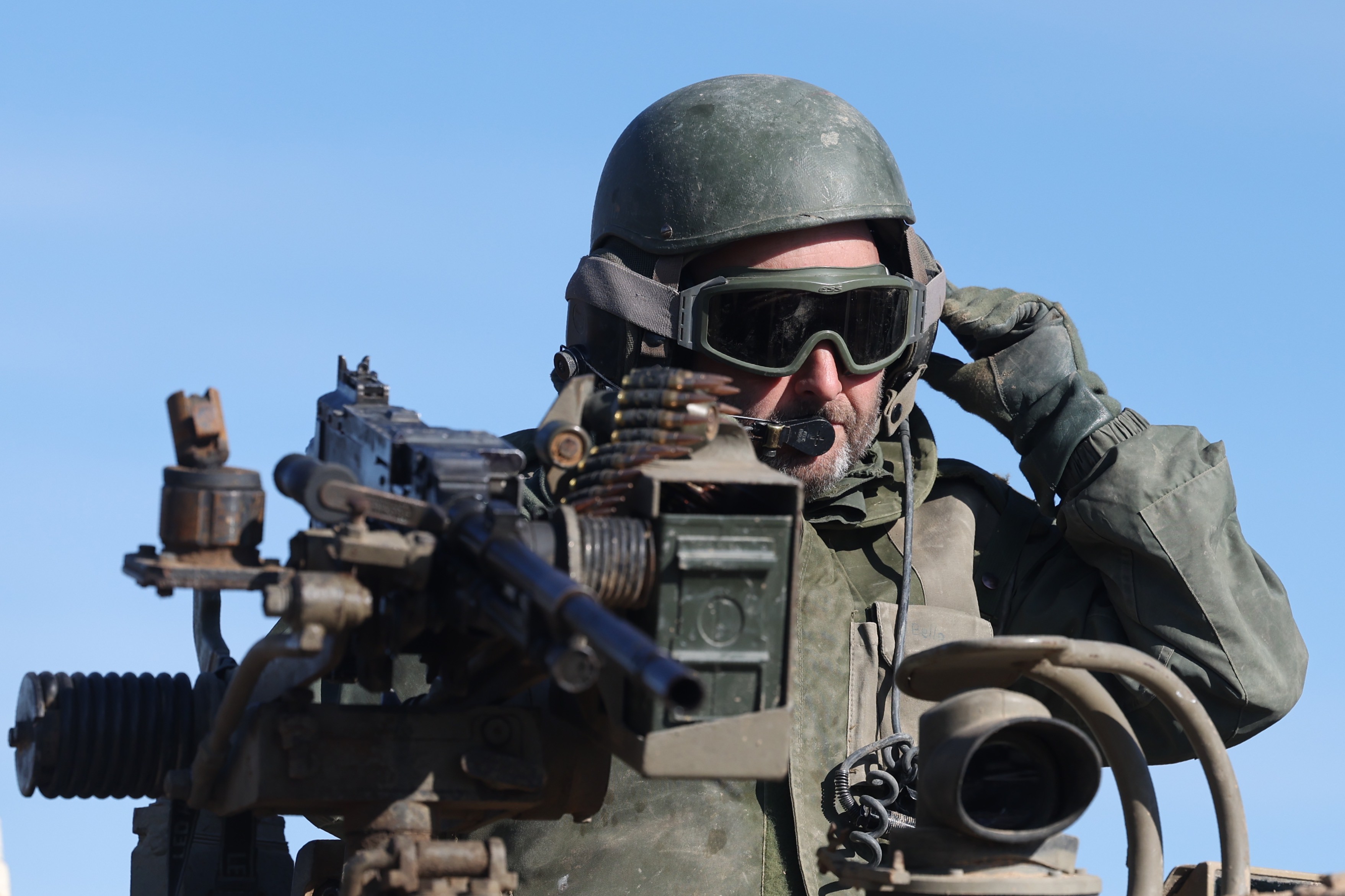 A heavily armoured Israeli soldier sits on their tank near the Gaza Strip, menacing gogglesm tank gun and helmet against a blue sky
