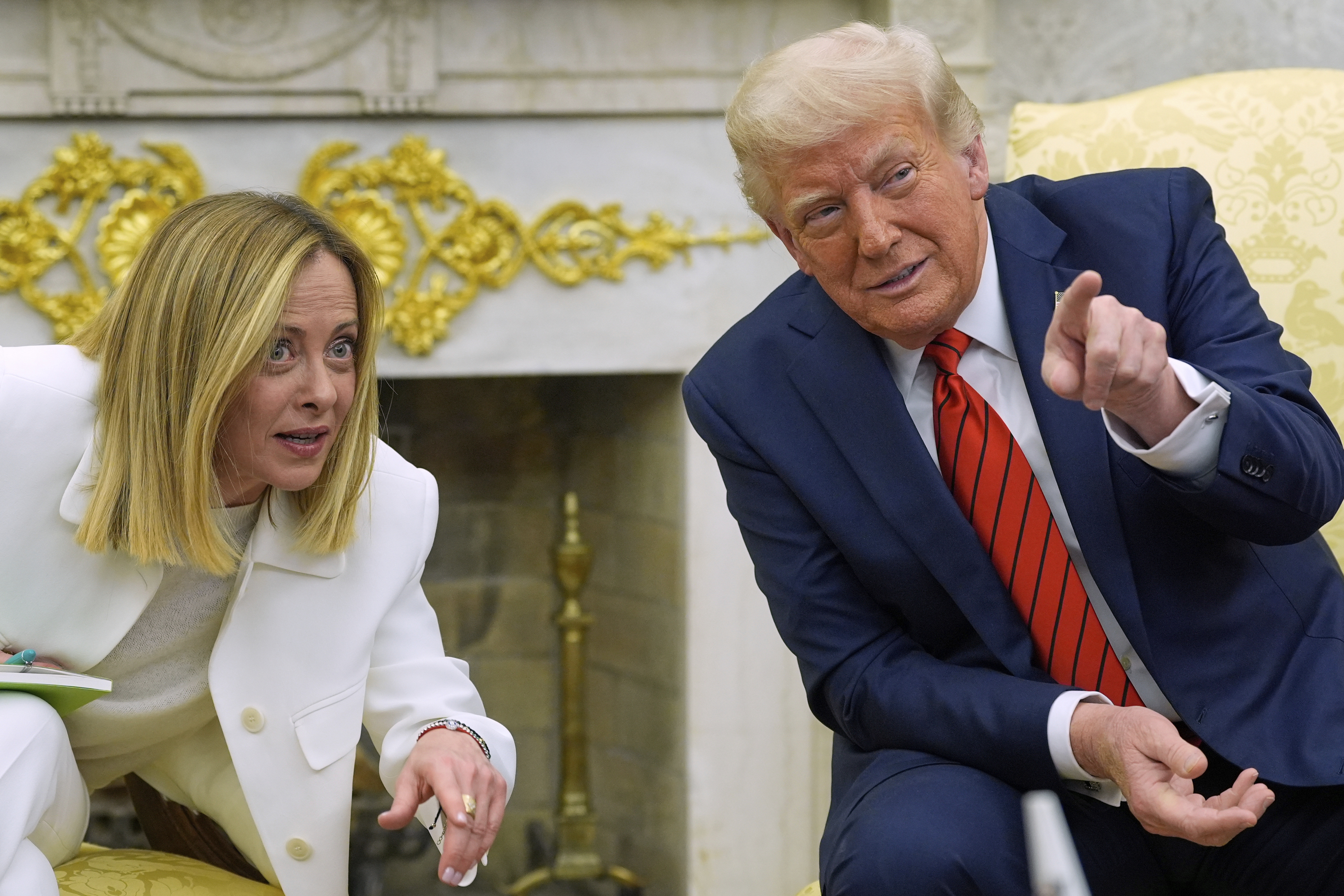Trump points at something while seated next to Giorgia Meloni.