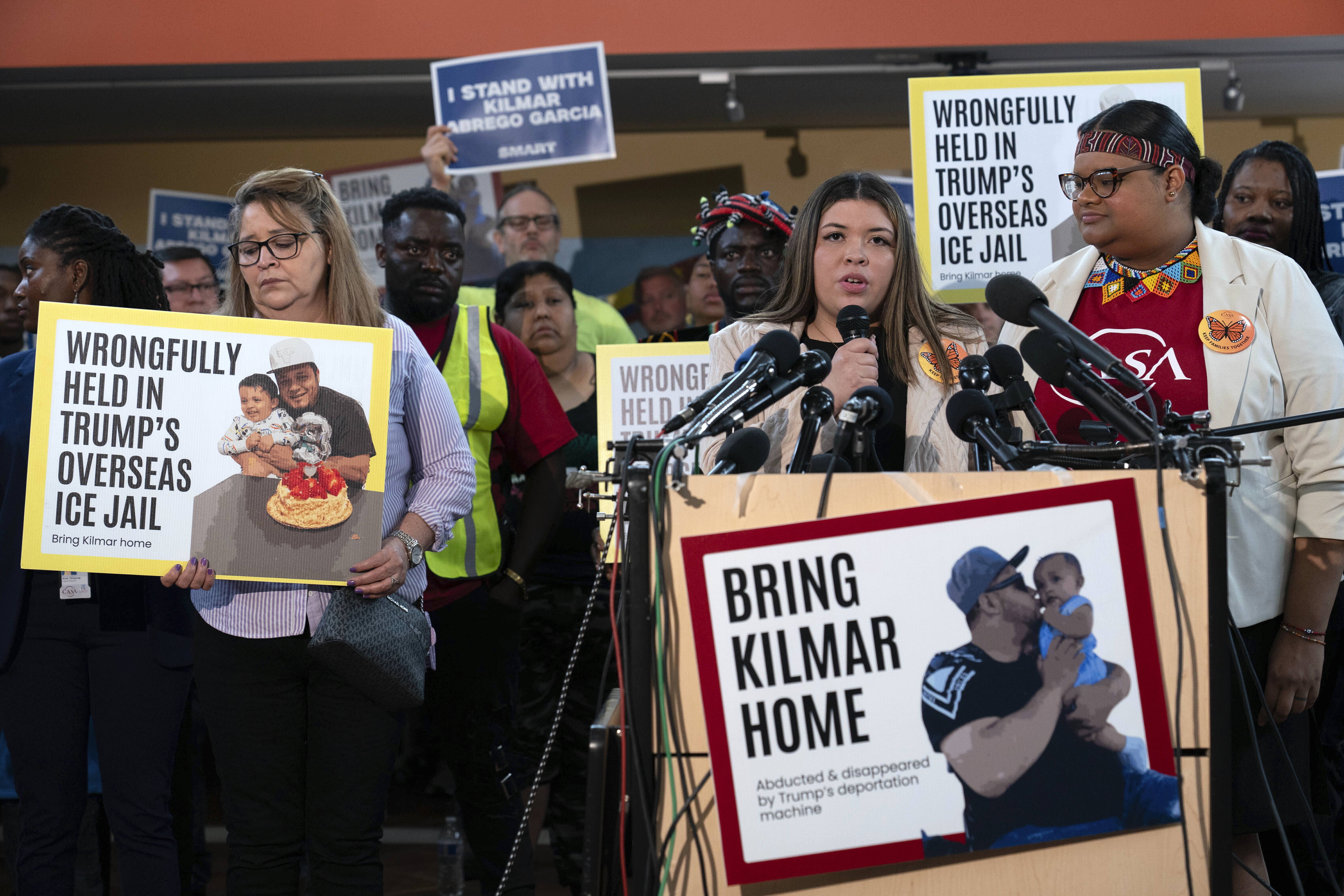 Jennifer Vaszquez Sura speaks behind a sign that reads "Bring Kilmar Home"