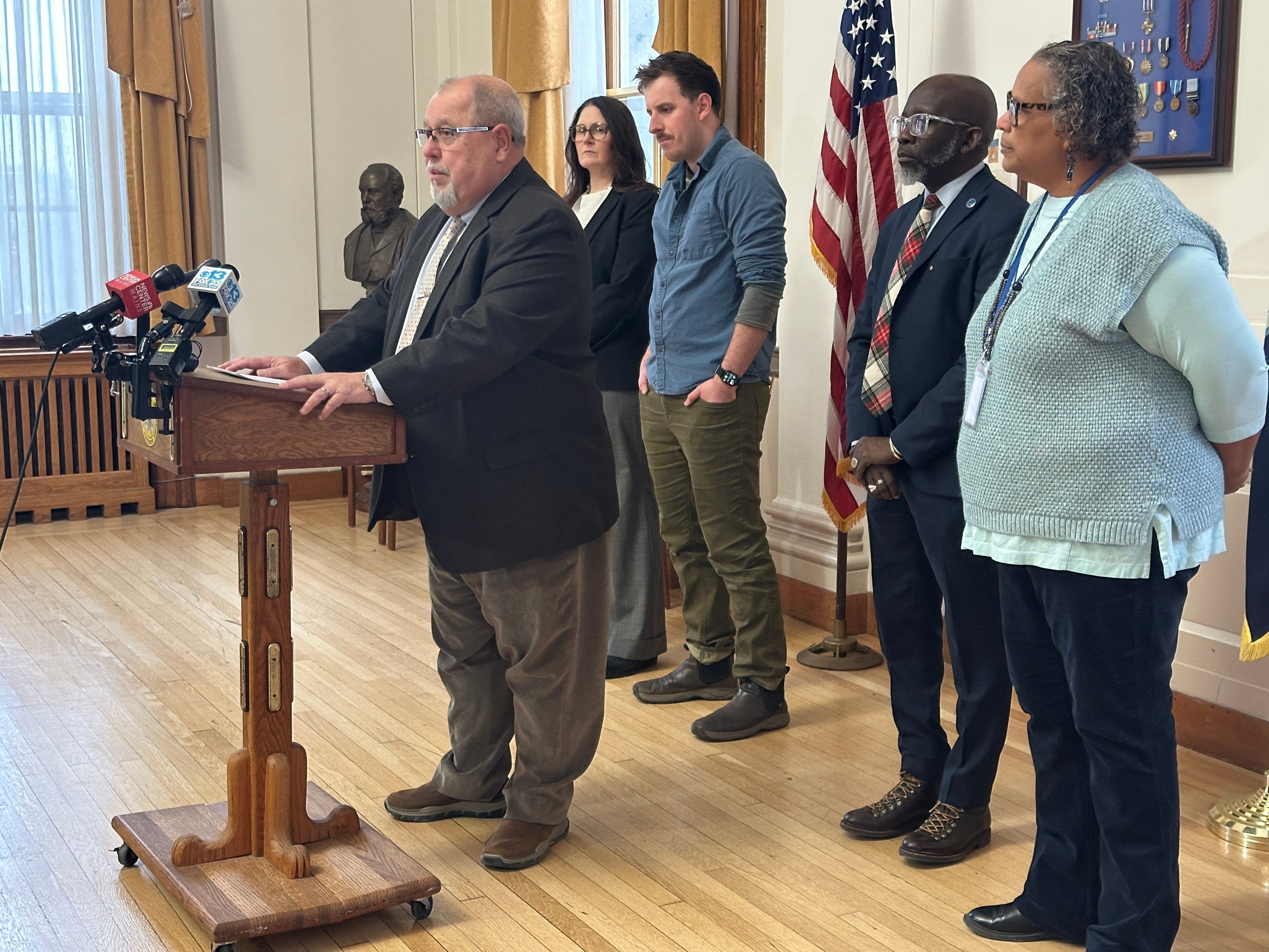 Mark Dion speaks at a podium, surrounded by city officials