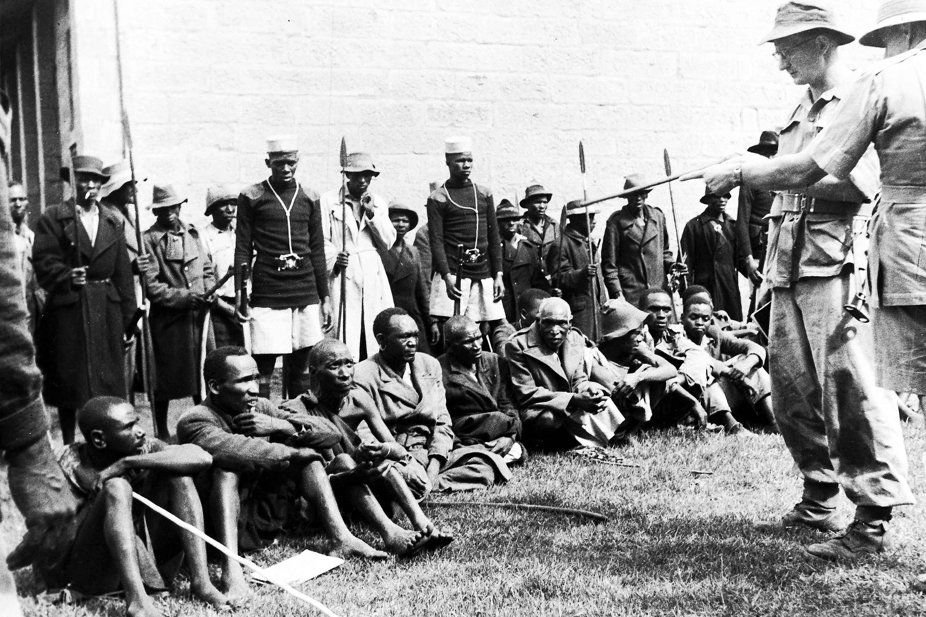 Guarded by members of the Lancashire Fusiliers, police and loyal Kikuyu spearmen, suspected members of the Mau Mau are questioned about the murder of two Europeans near Gilgil, Kenya, on Jan. 8, 1953. (AP Photo, File)