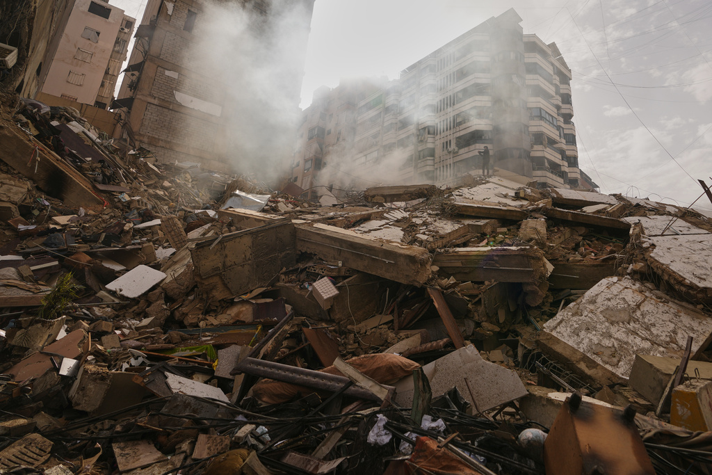 A man stands atop the rubble of a building destroyed in an Israeli airstrike as a bulldozer clears debris in Dahiyeh